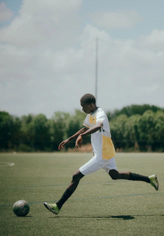Soccer player kicks the ball on a green field.