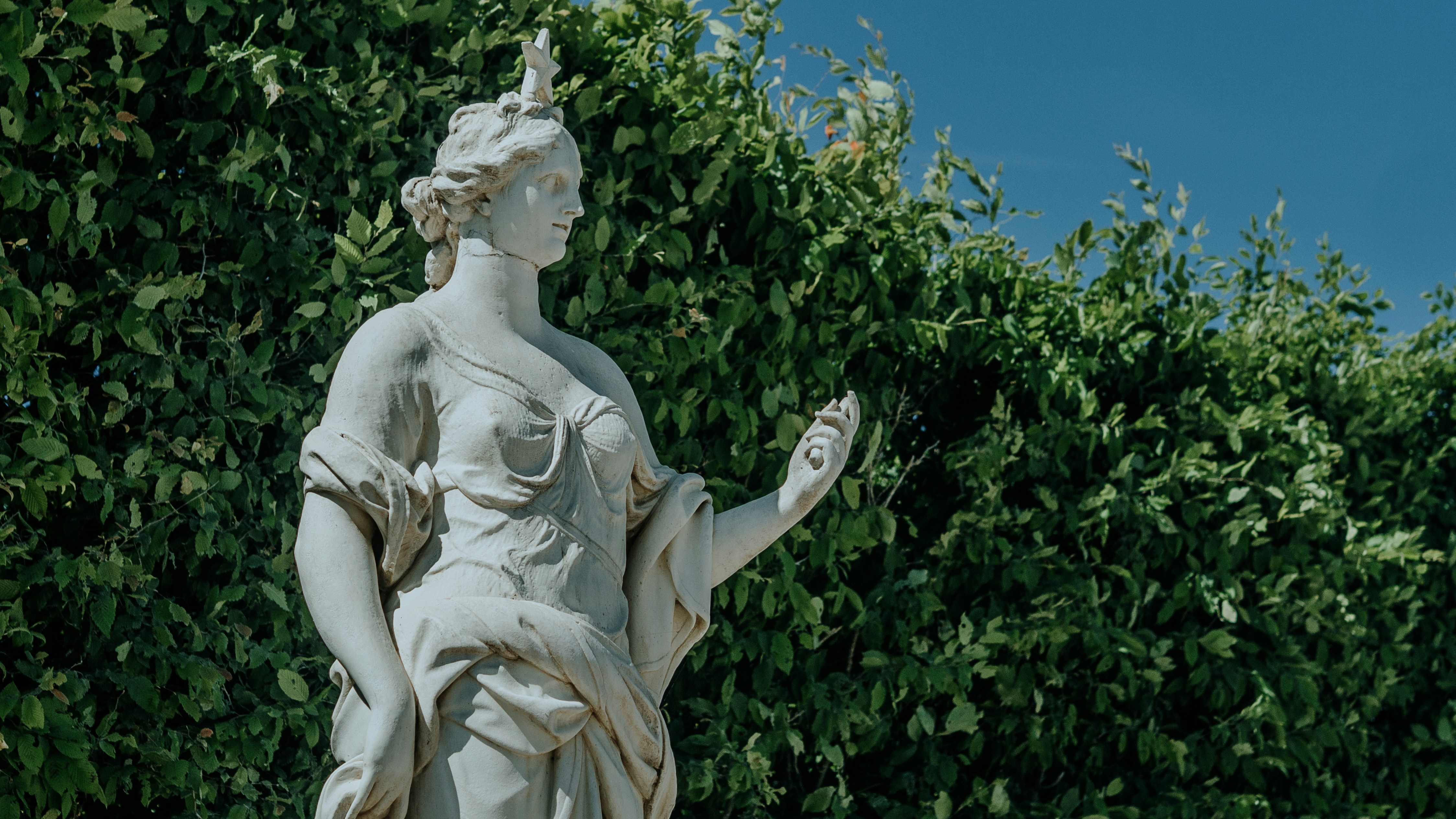 Una estatua de piedra se encuentra frente a una exuberante vegetación.
