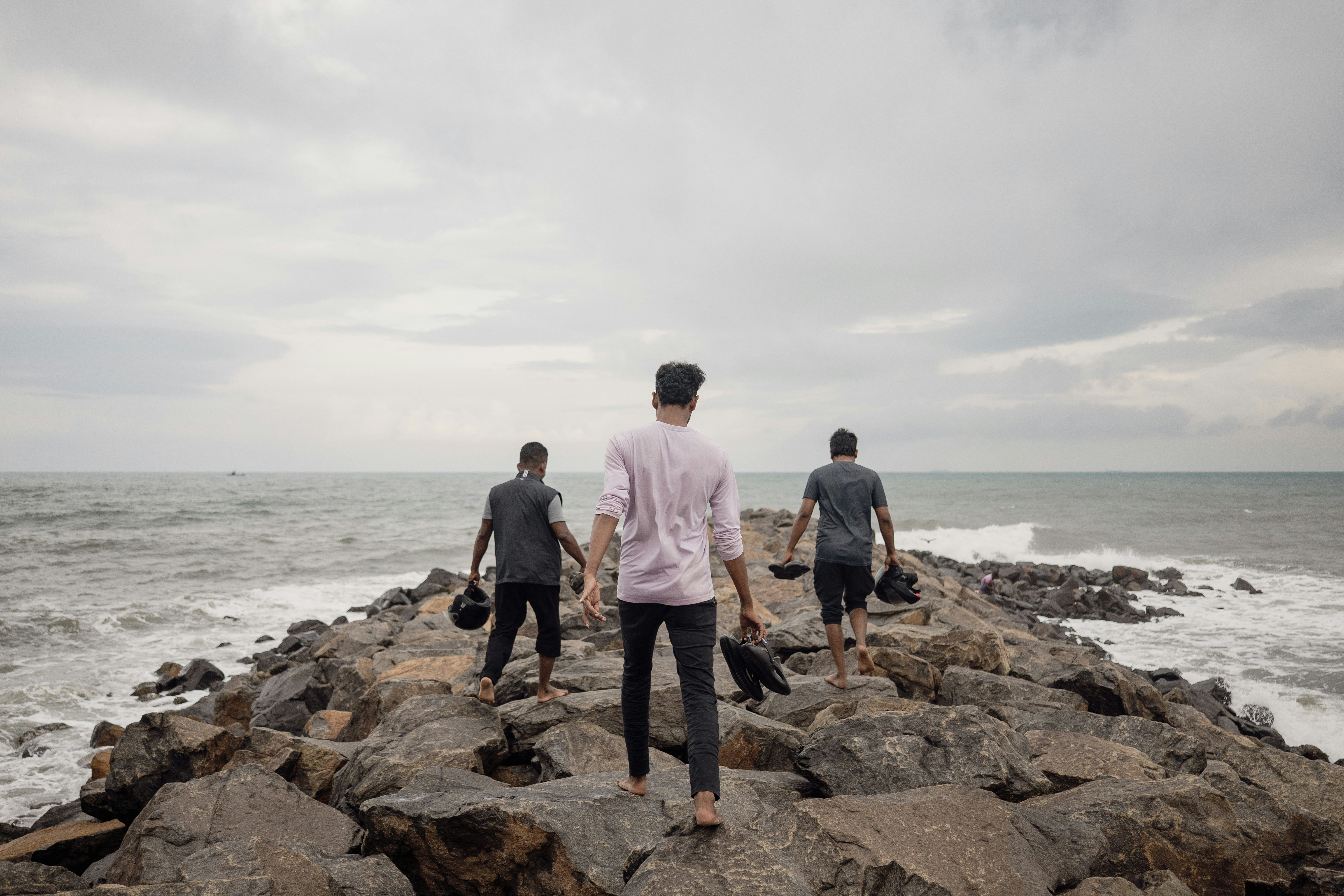 Three men walk towards the sea.