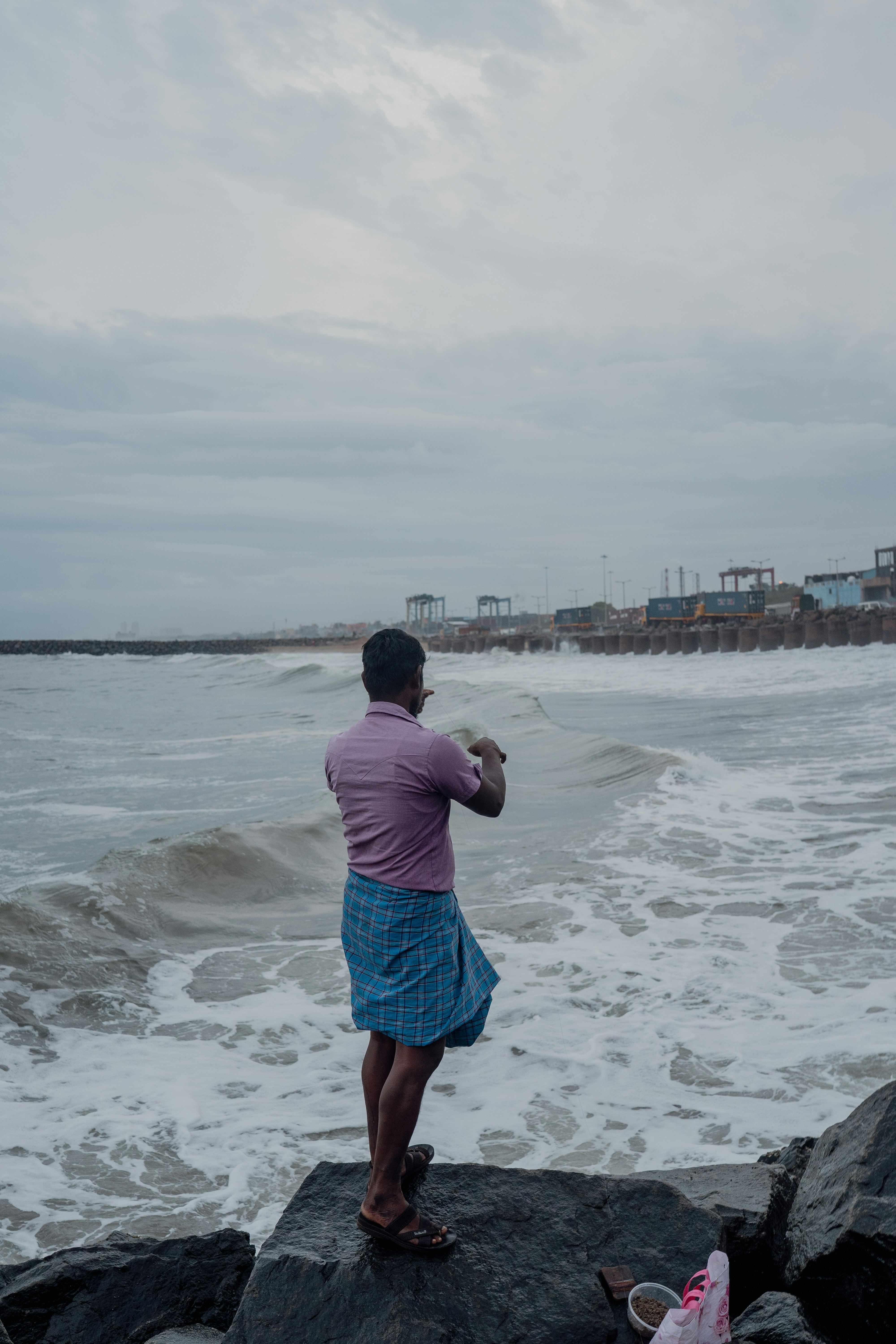 A man stands on rocks by a stormy sea.