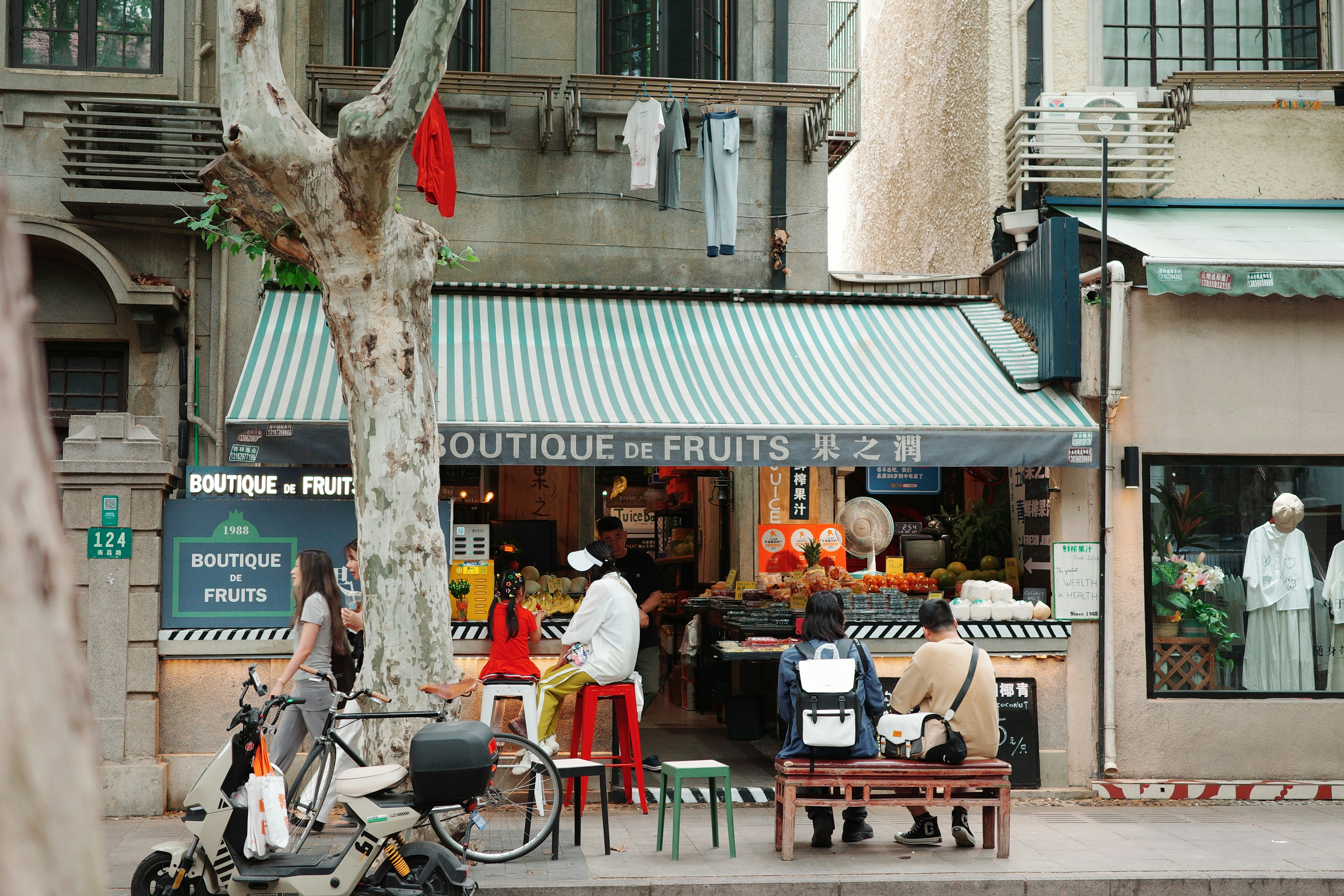 A fruit shop with people and a scooter.
