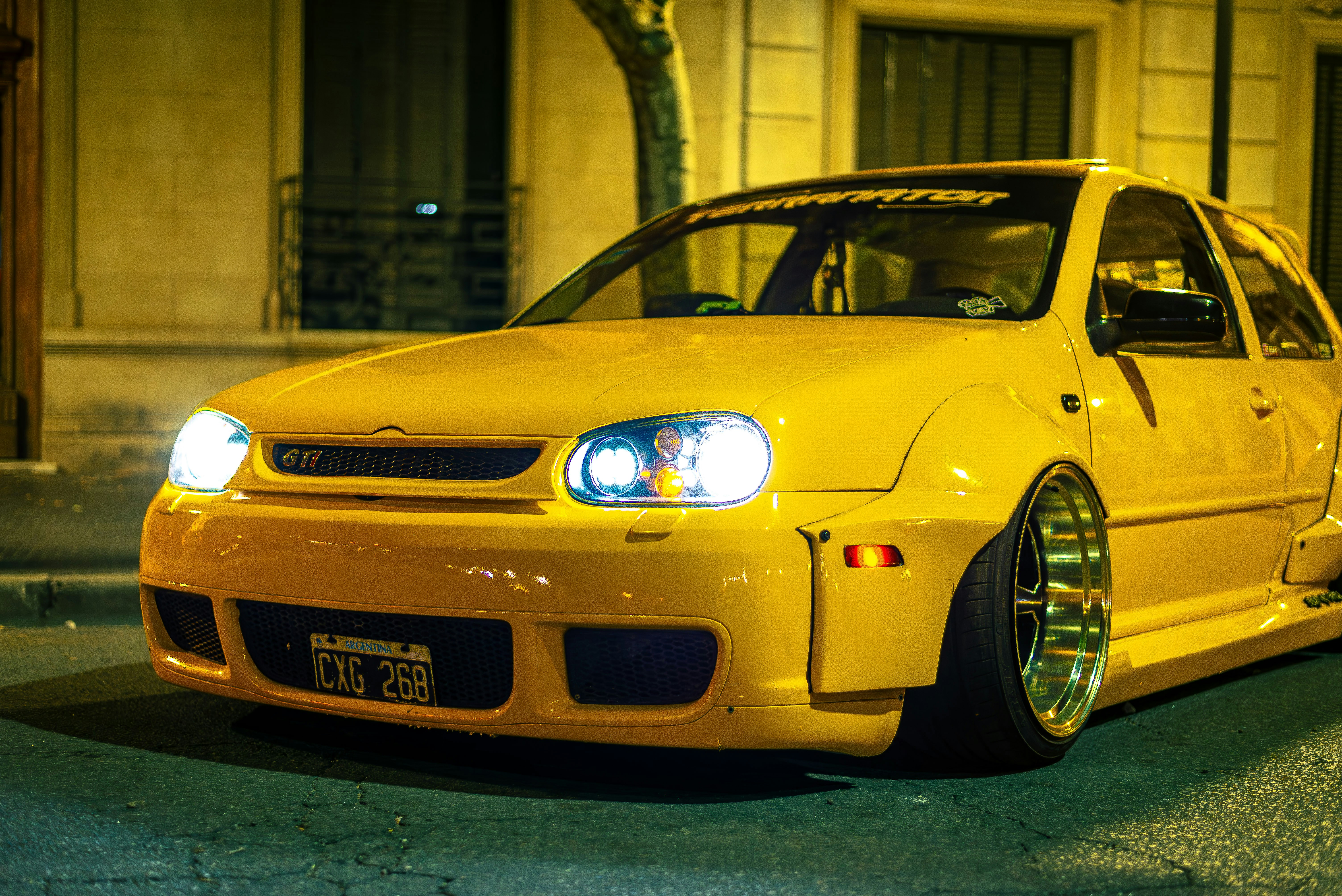 A modified, yellow car is parked on the street.