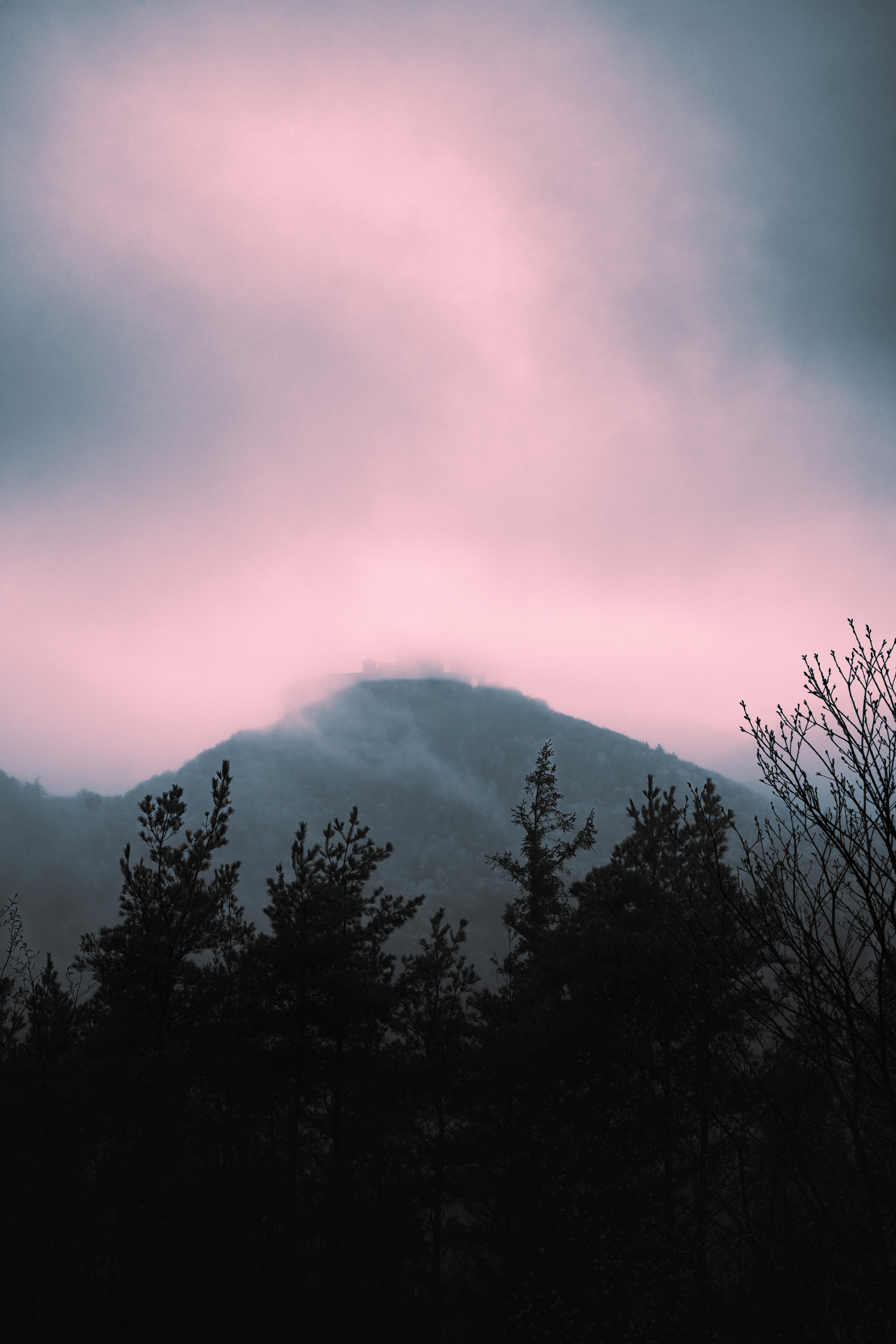 Mountain shrouded in mist under a pink sky.