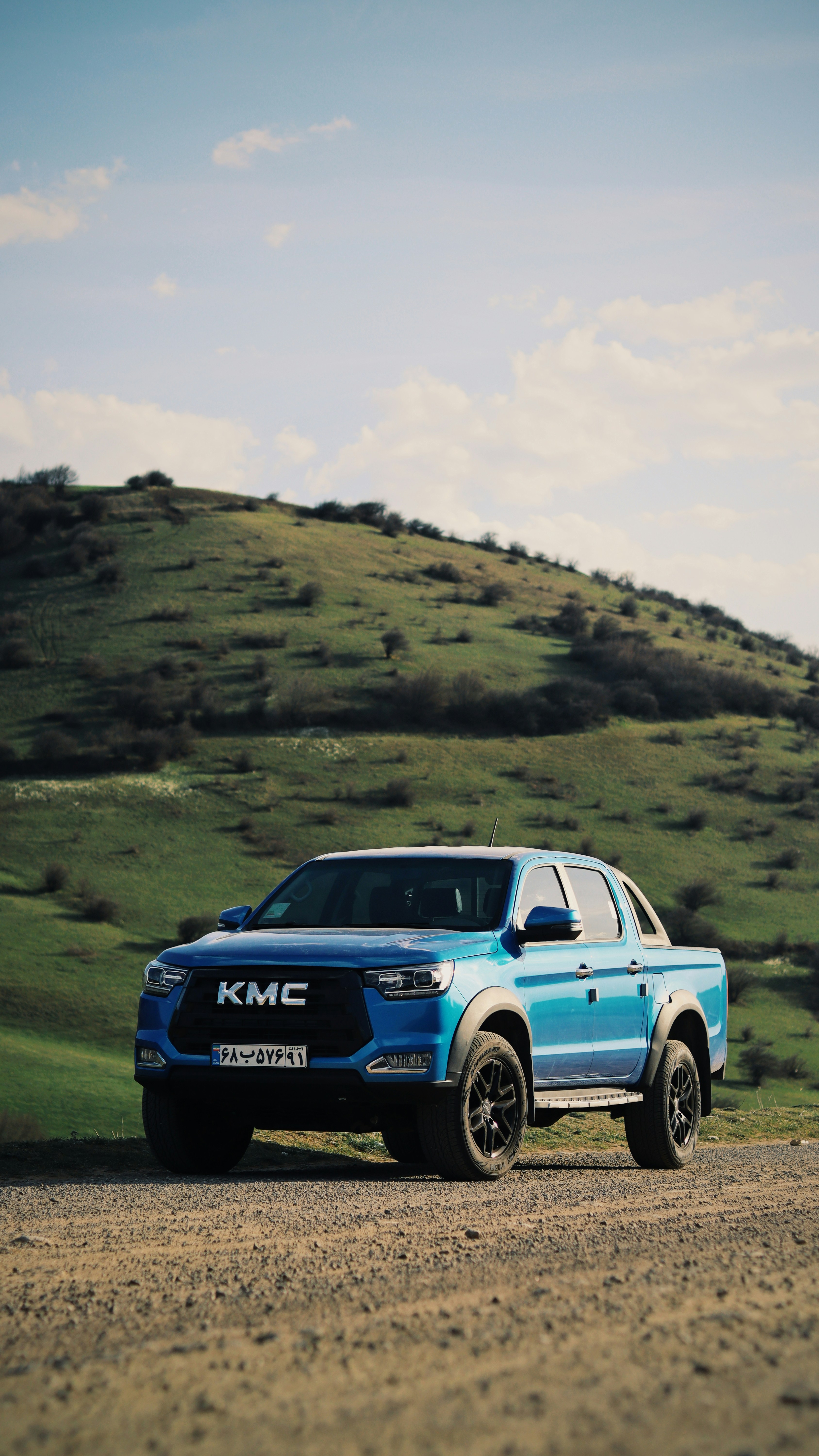 A blue kmc truck parks near a hill.