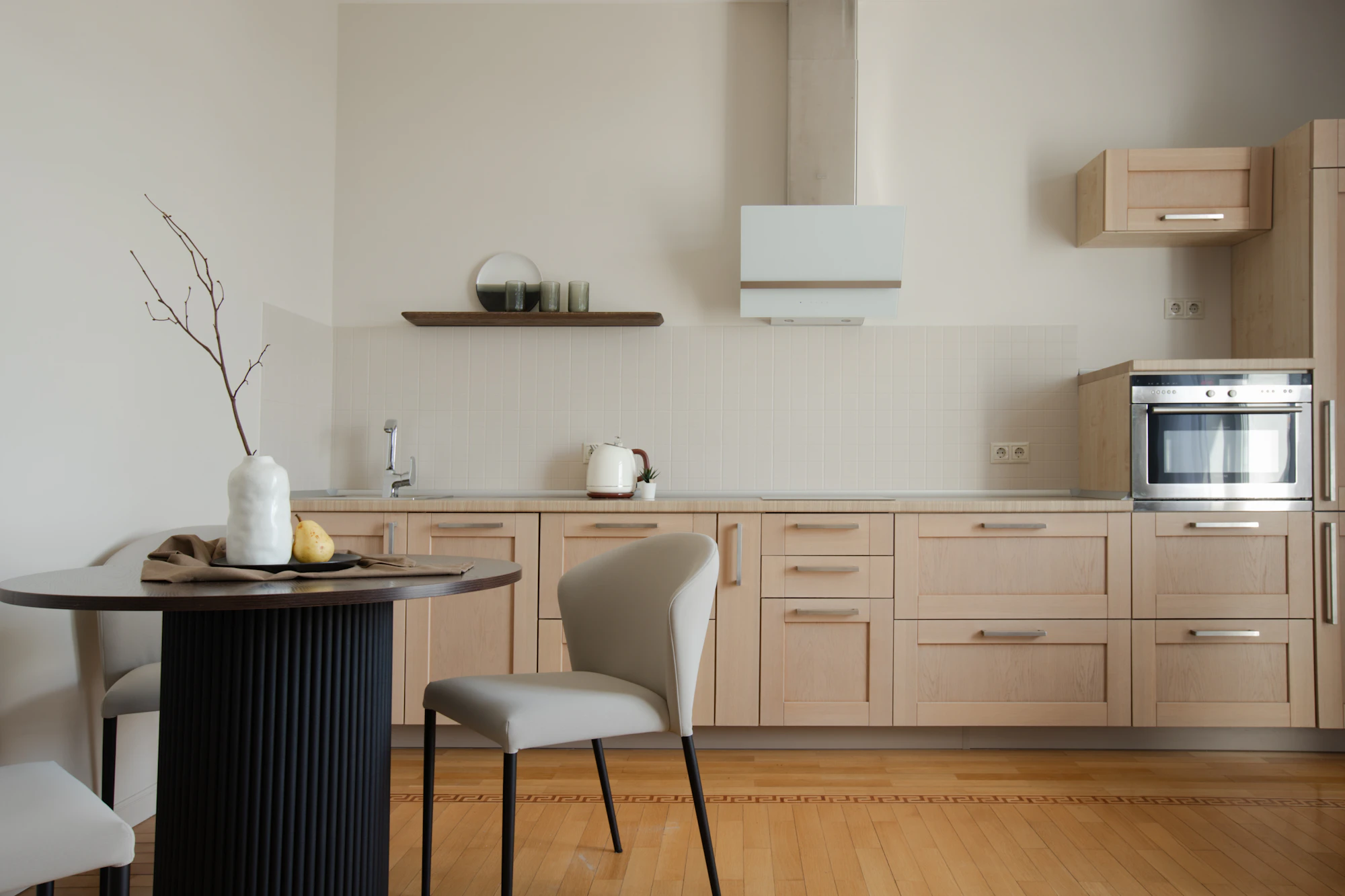 Bright contemporary kitchen with pale wood cabinetry, white tiled backsplash, integrated appliances and a small dining area.