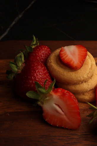 Strawberries and cookies rest on a wooden board.
