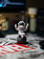 Astronaut figurine gives peace signs on a small moon.