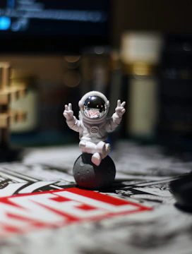 Astronaut figurine gives peace signs on a small moon.