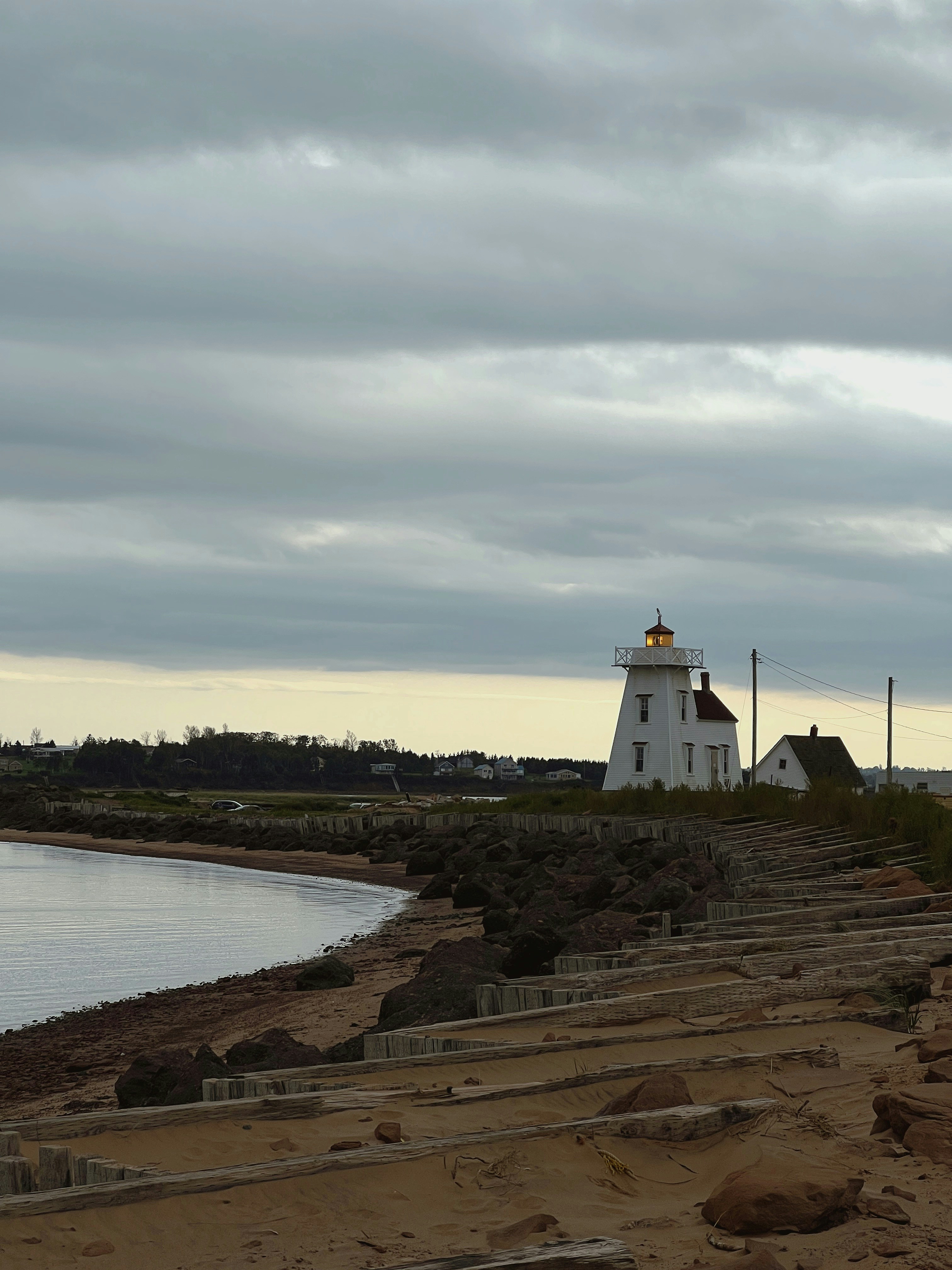 A lighthouse stands on the coast under a cloudy sky.