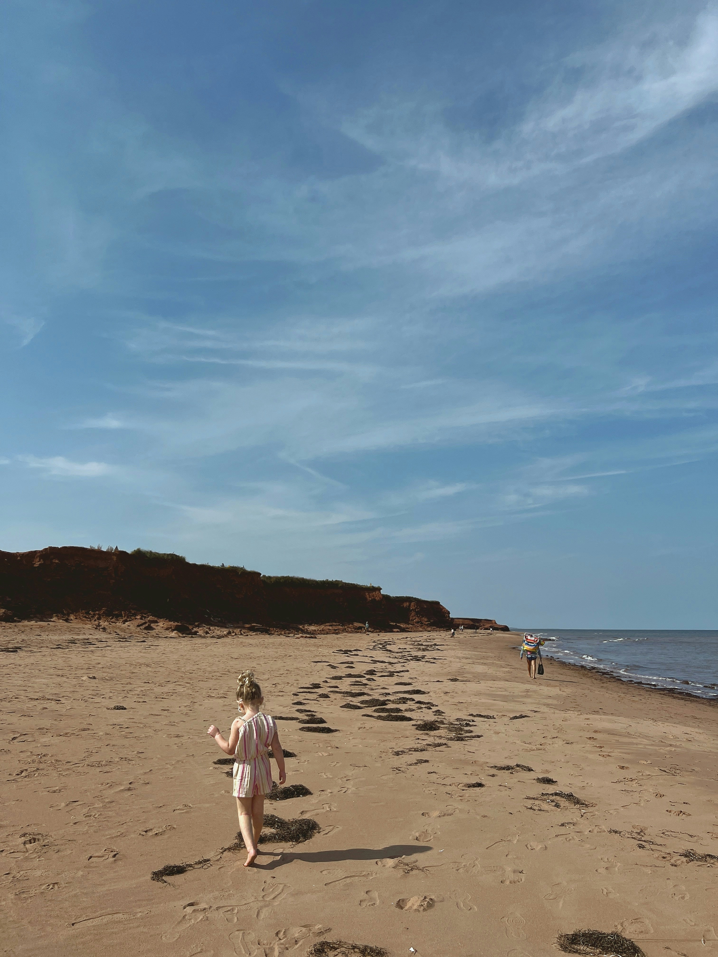A girl walks along the beach under the blue sky.