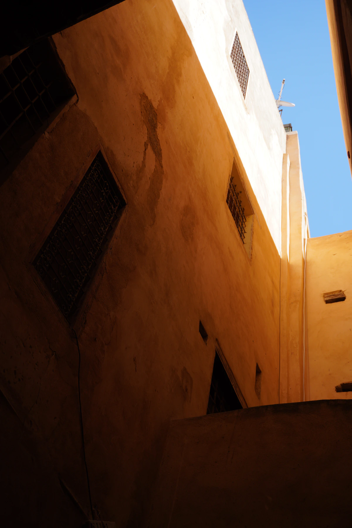 Tall historic buildings rising above a narrow sunlit alley in Fès