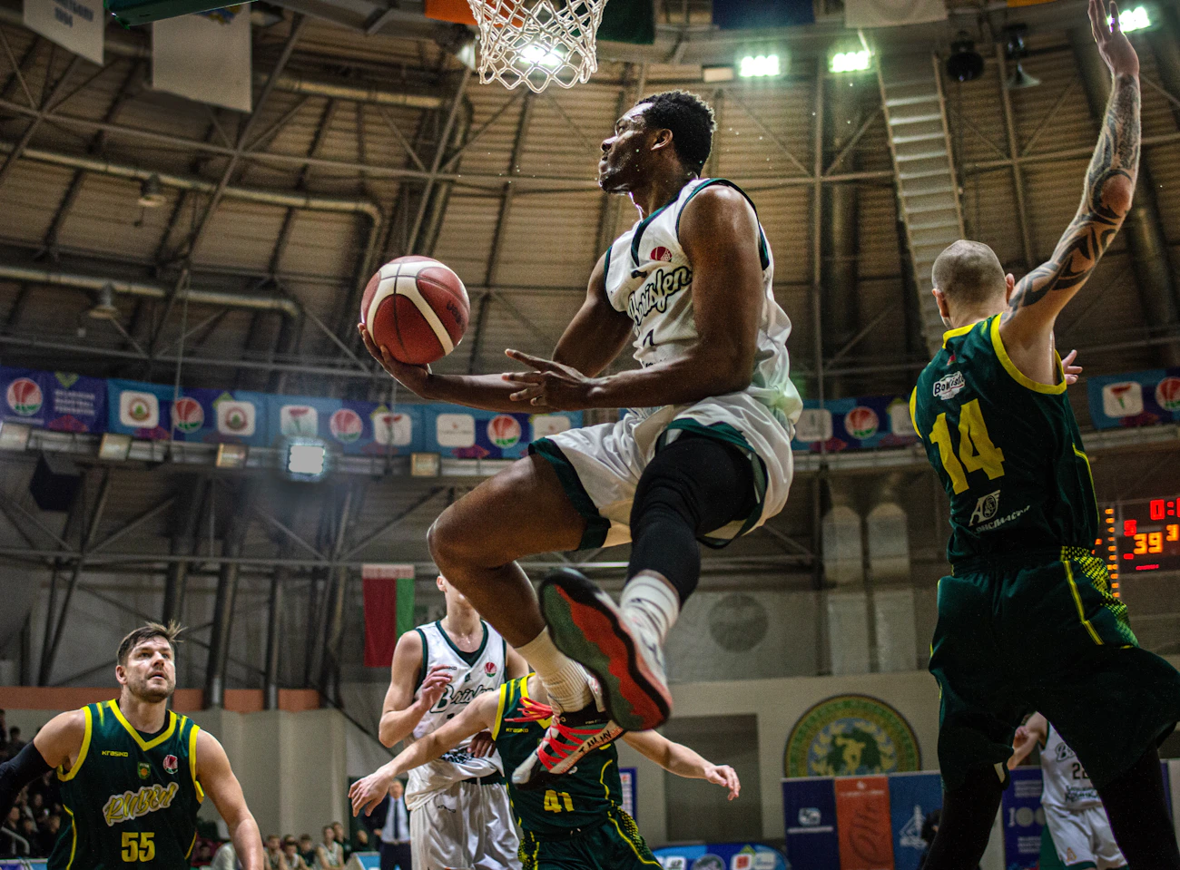 Basketball player rising toward the hoop as defenders contest a dunk