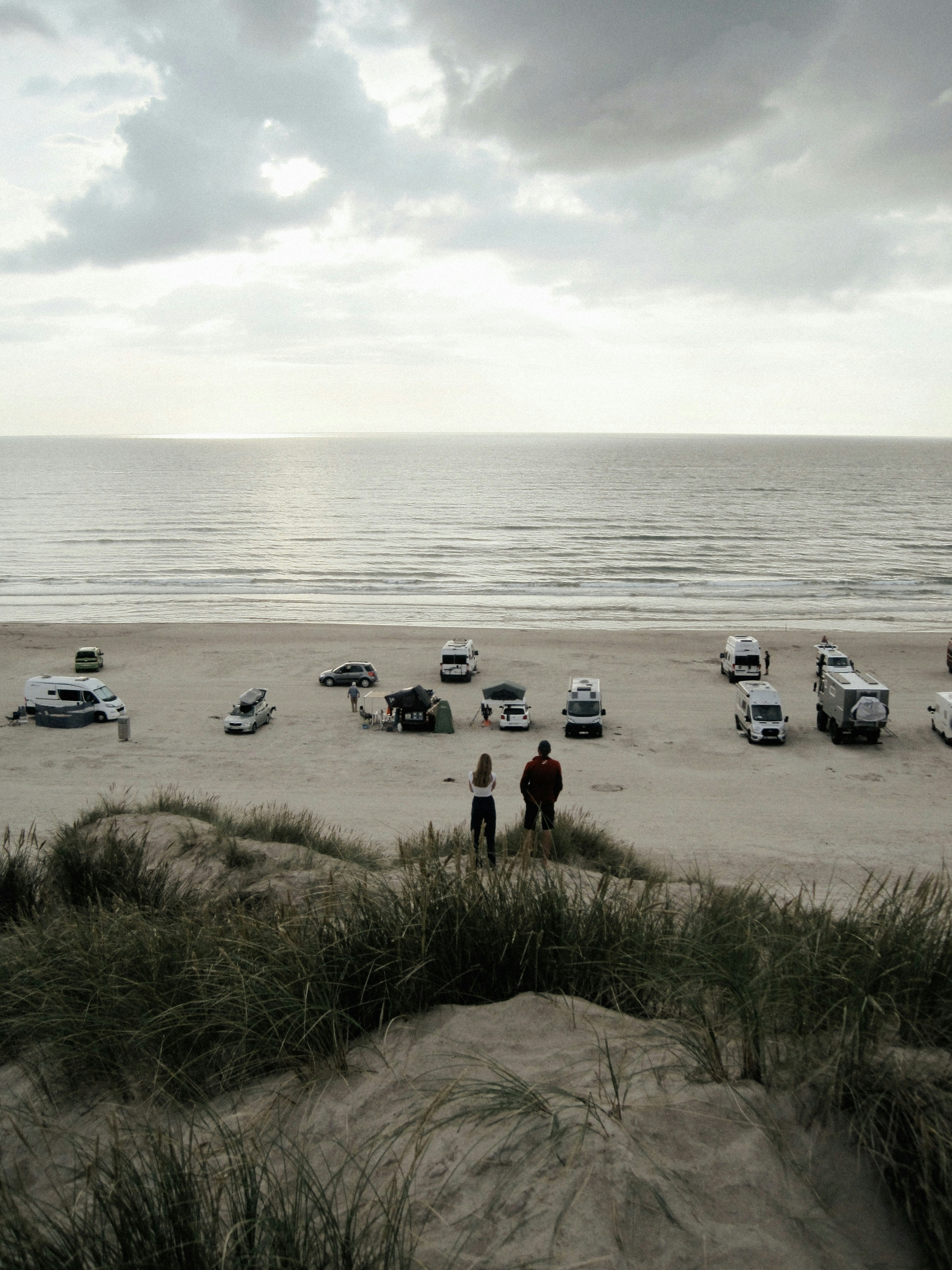 La gente sta in piedi su una duna, guardando la spiaggia.