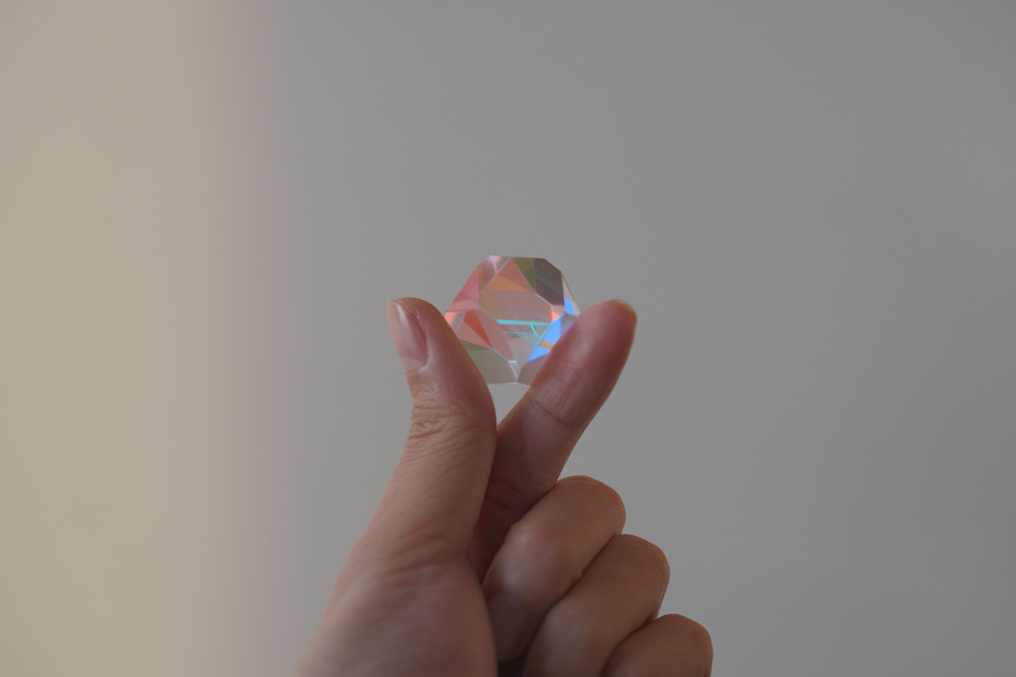 A hand holds a colorful, reflective gem.