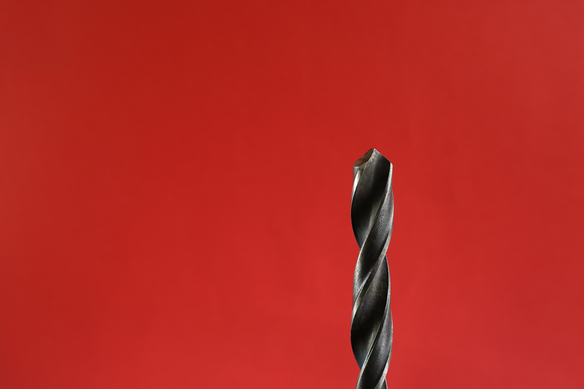 A drill bit is shown against a red background.
