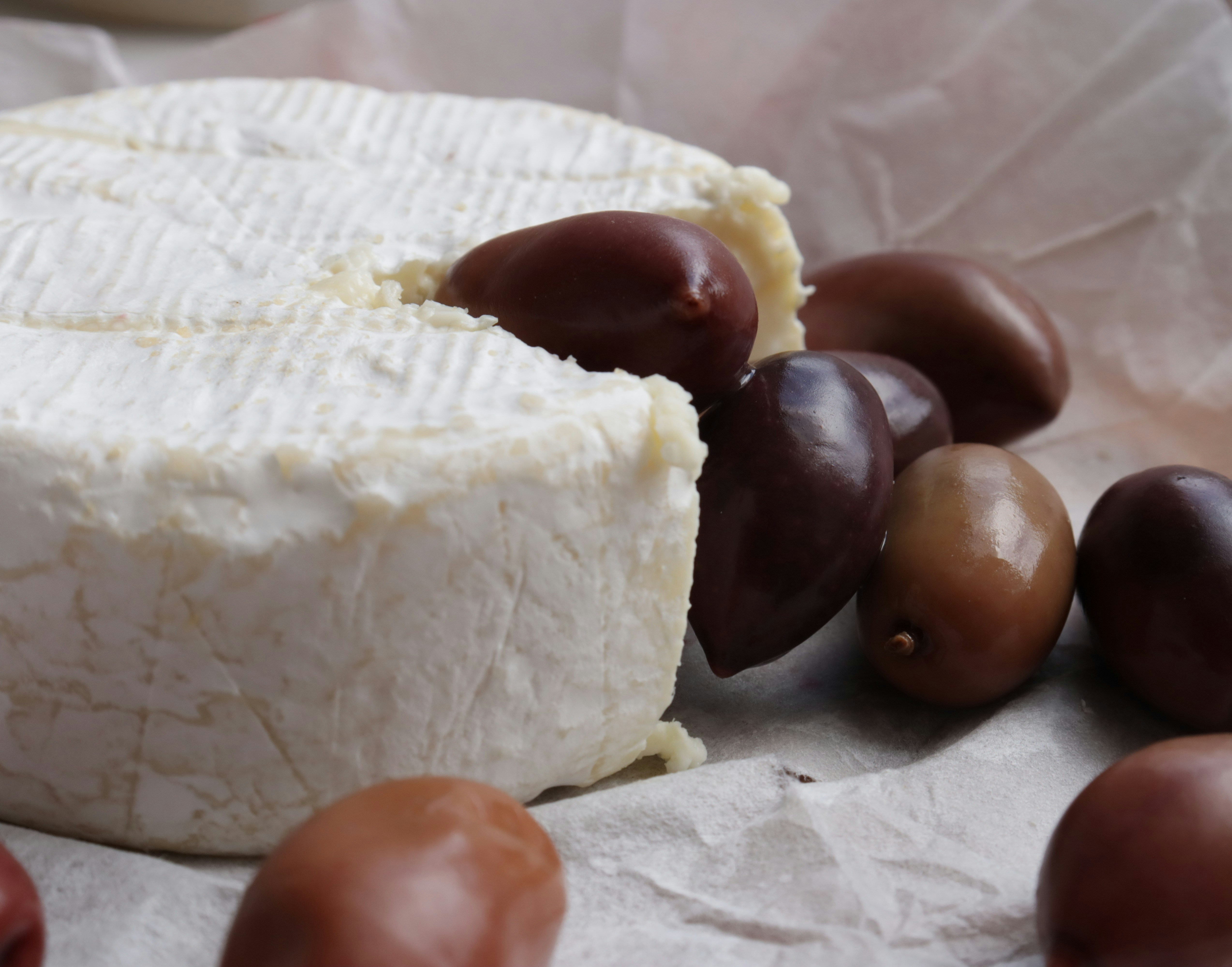 Cheese wheel with olives on parchment paper.