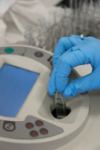 Gloved hand inserts a vial into a scientific instrument.