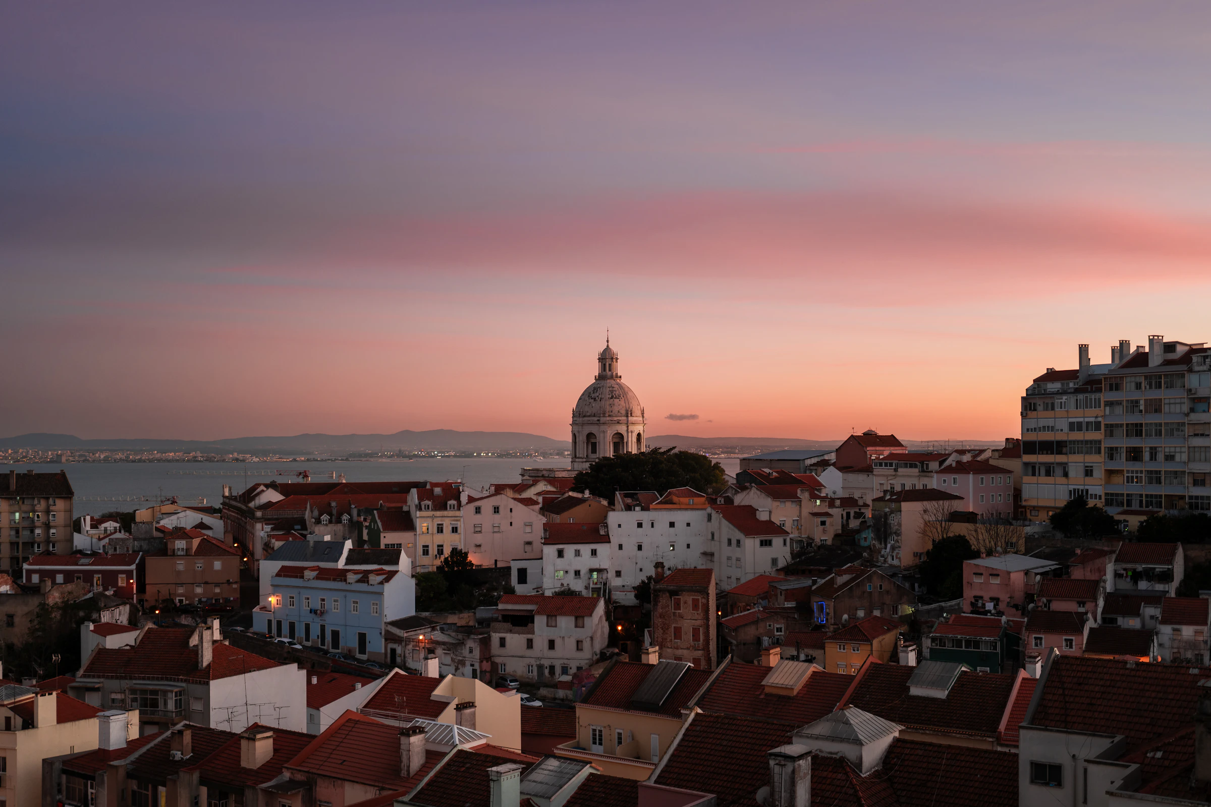 Sunset over colorful Lisbon rooftops with ocean in the distance