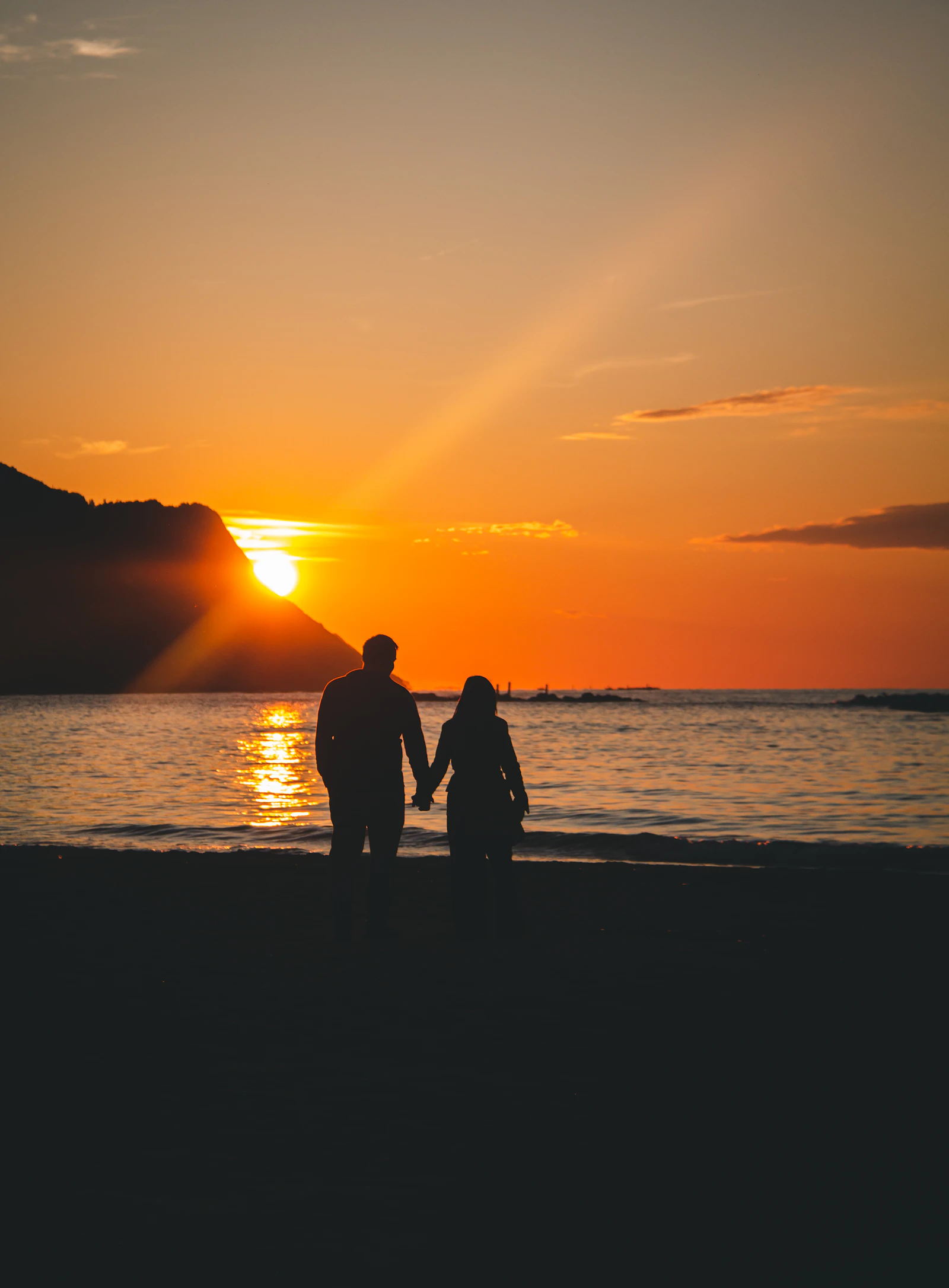 Couple holding hands while walking on a beach at sunset