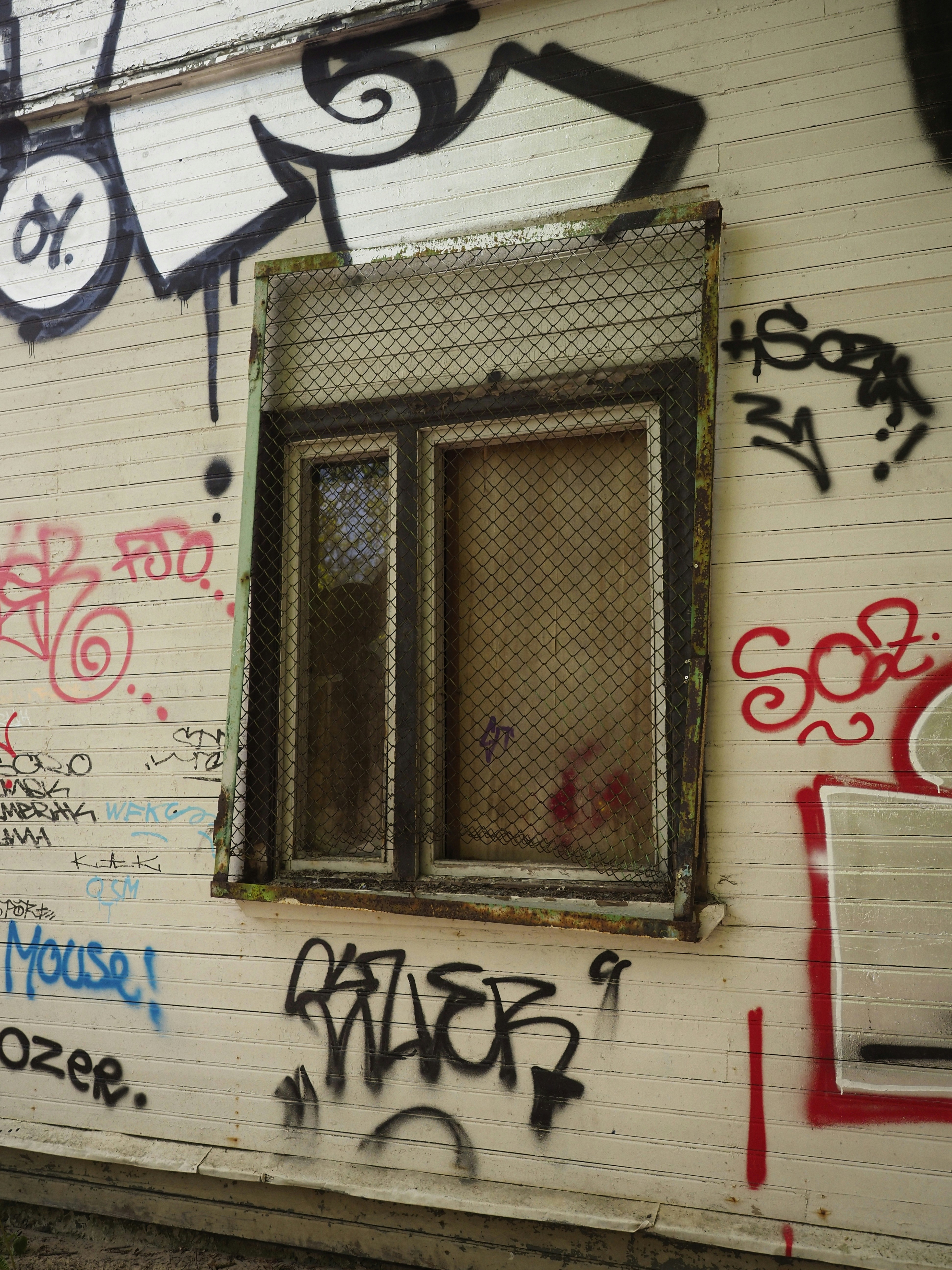 Graffiti bedeckt eine Wand mit einem abgeschirmten Fenster.