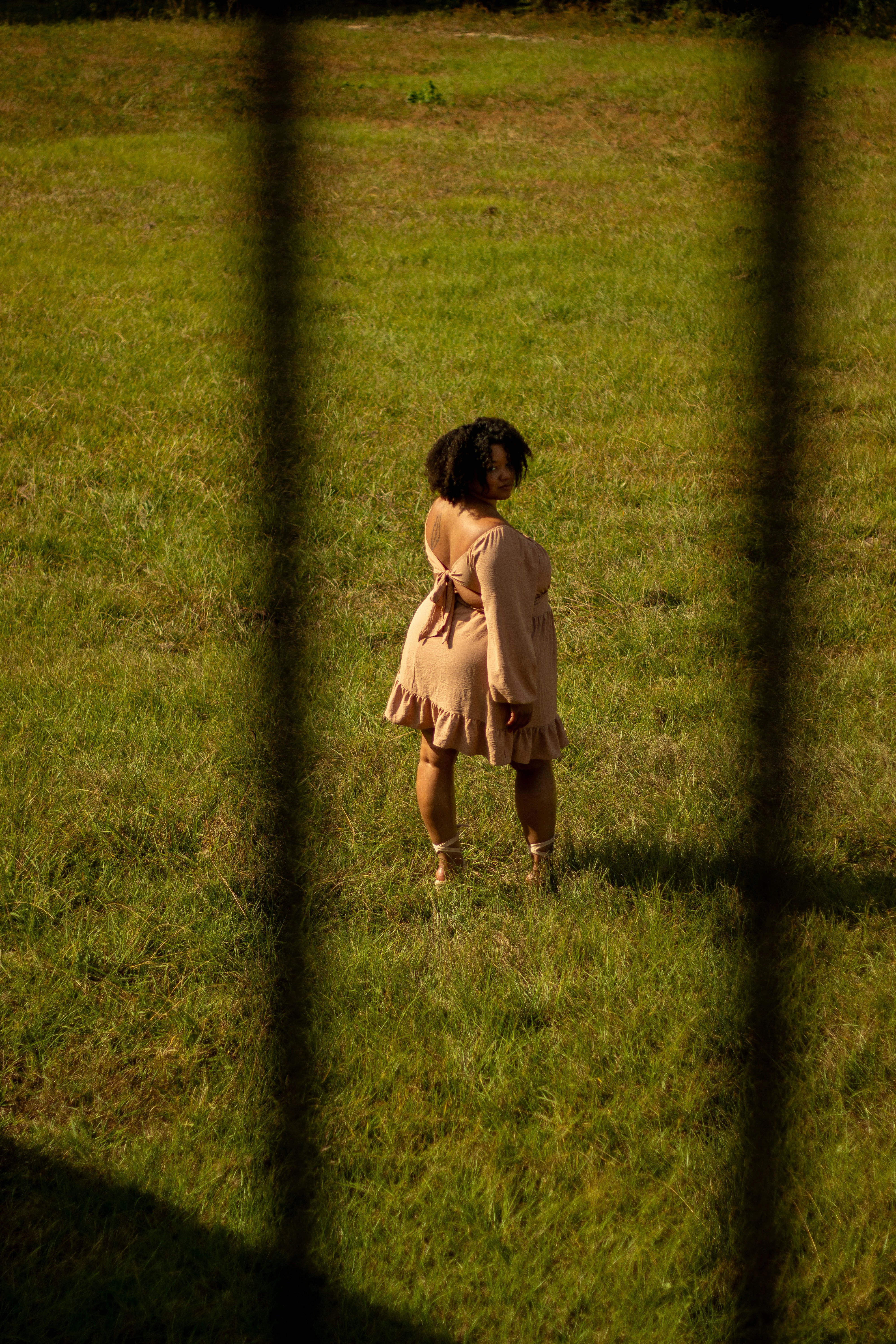 Woman stands in a field, viewed through shadows.