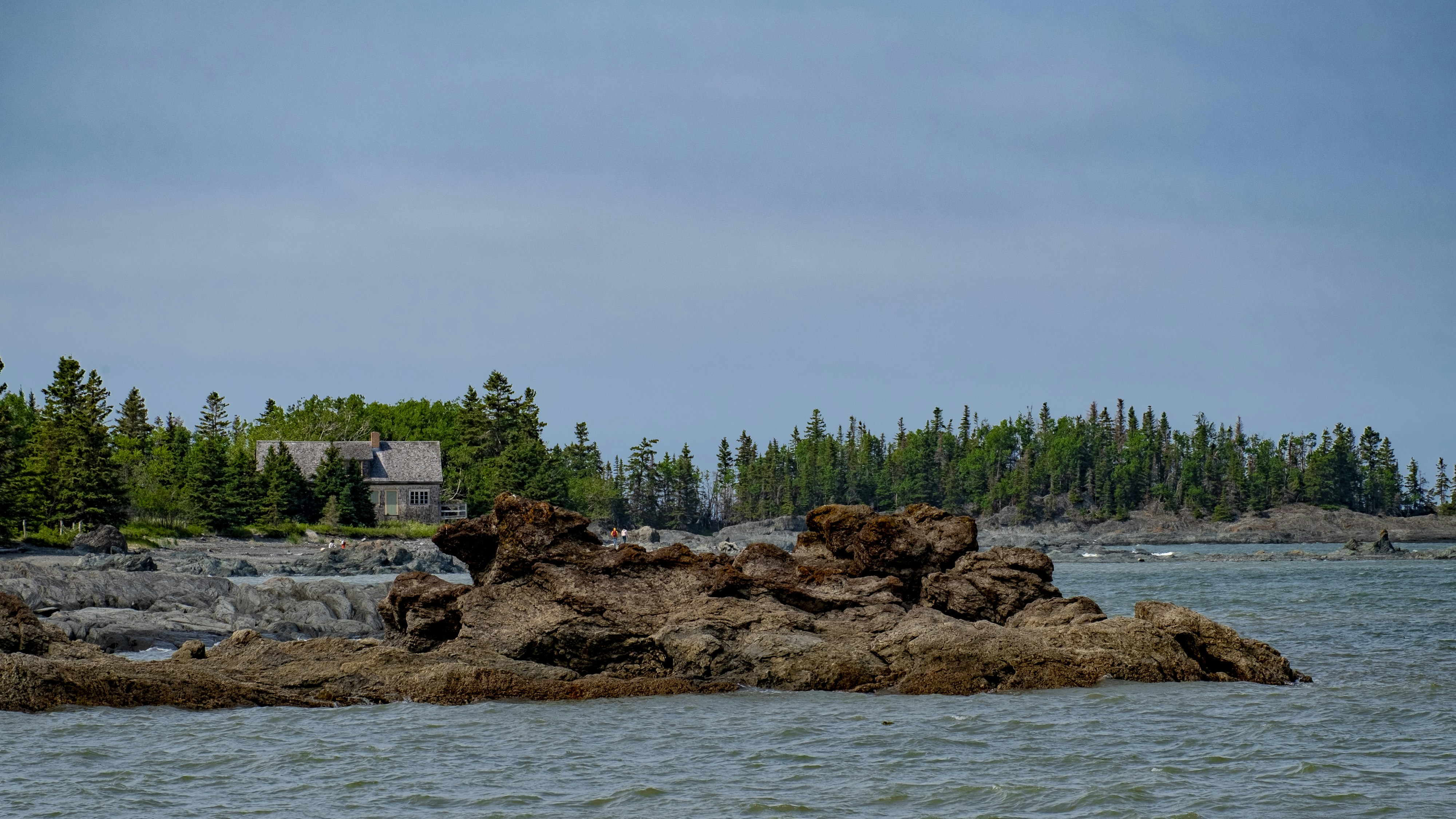Rocks and trees line the coast under a cloudy sky.