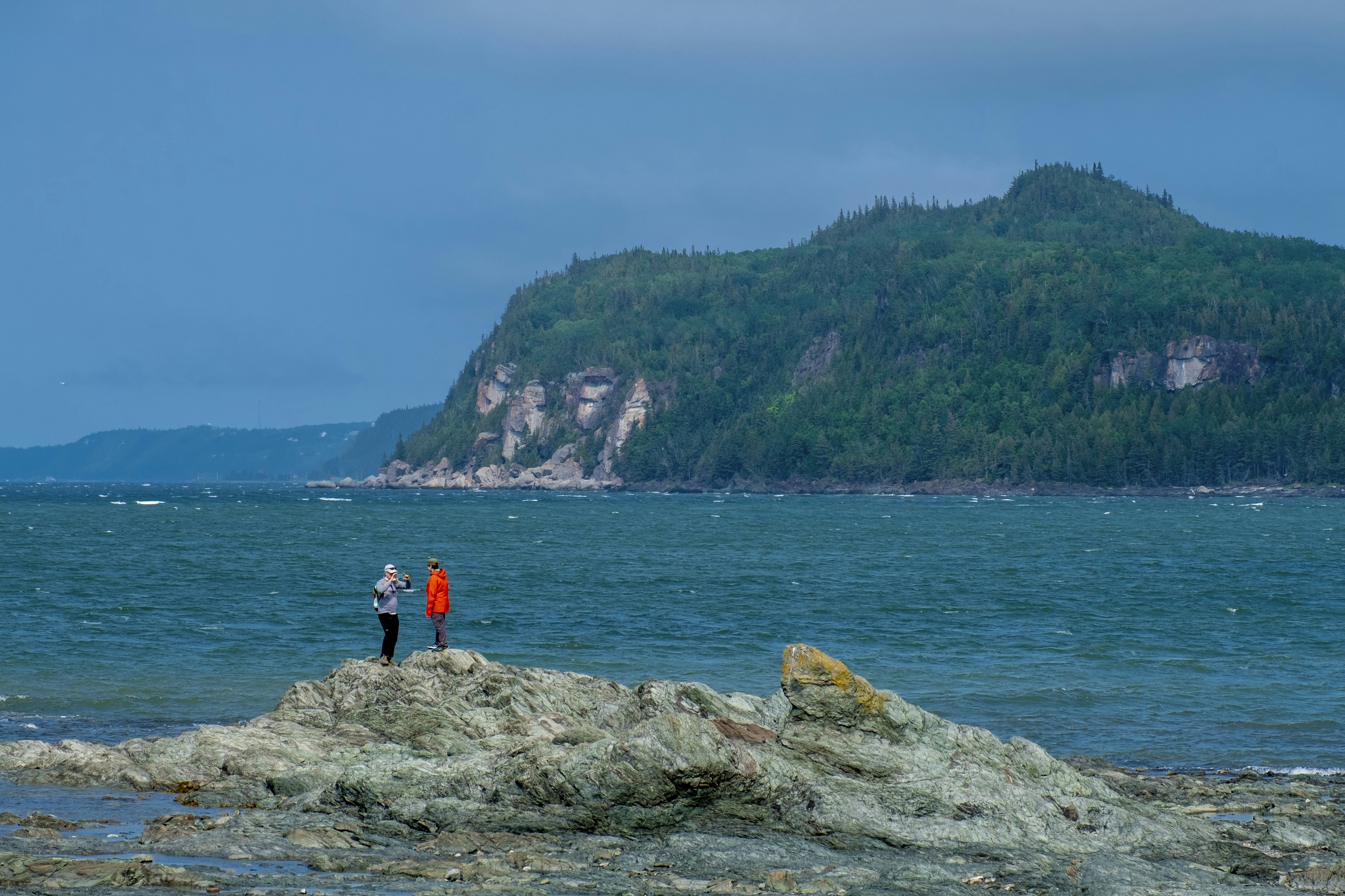 Two people stand on a rock, gazing at the view.