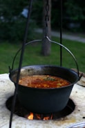 Soup is being cooked in a large hanging pot.