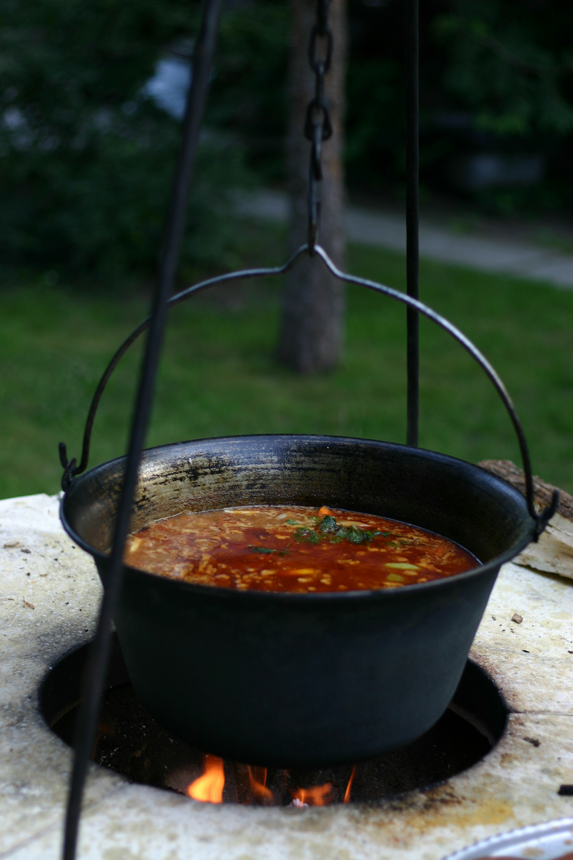 Soup is being cooked in a large hanging pot.