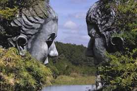 Two stone faces emerge from greenery.
