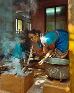 Woman cooks food in a traditional, smoky kitchen.