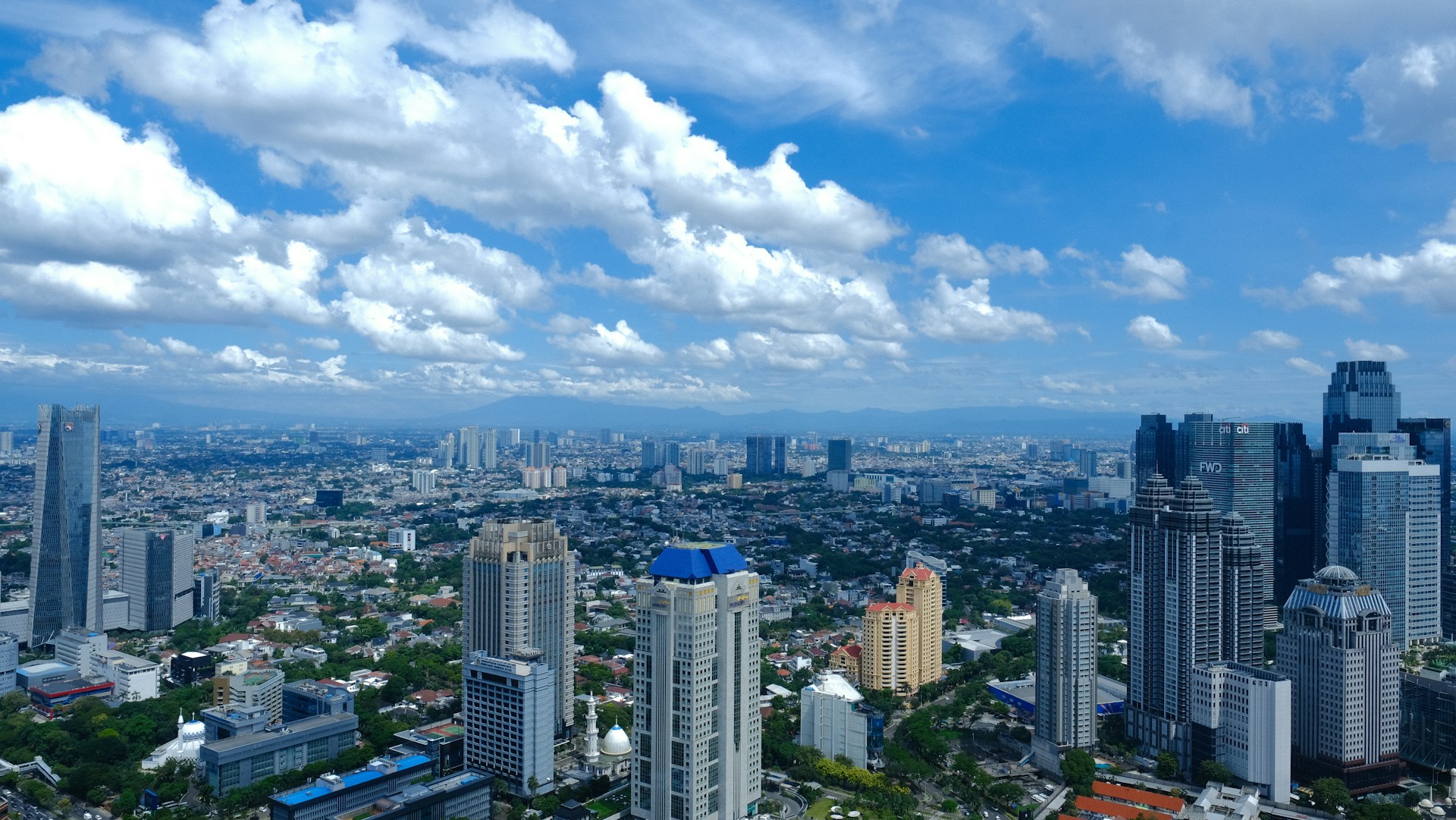 Cityscape under a bright blue sky with fluffy clouds.