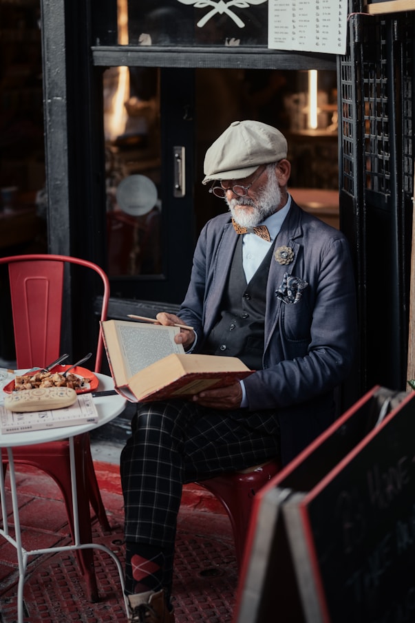 Stylish elderly gentleman reads a book at a cafe.