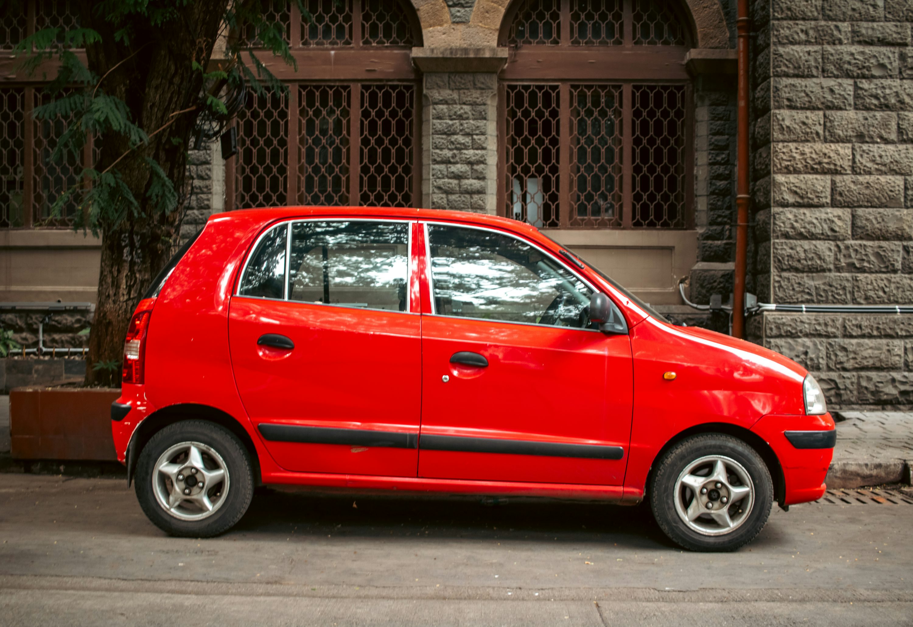 A red car is parked beside a stone building.
