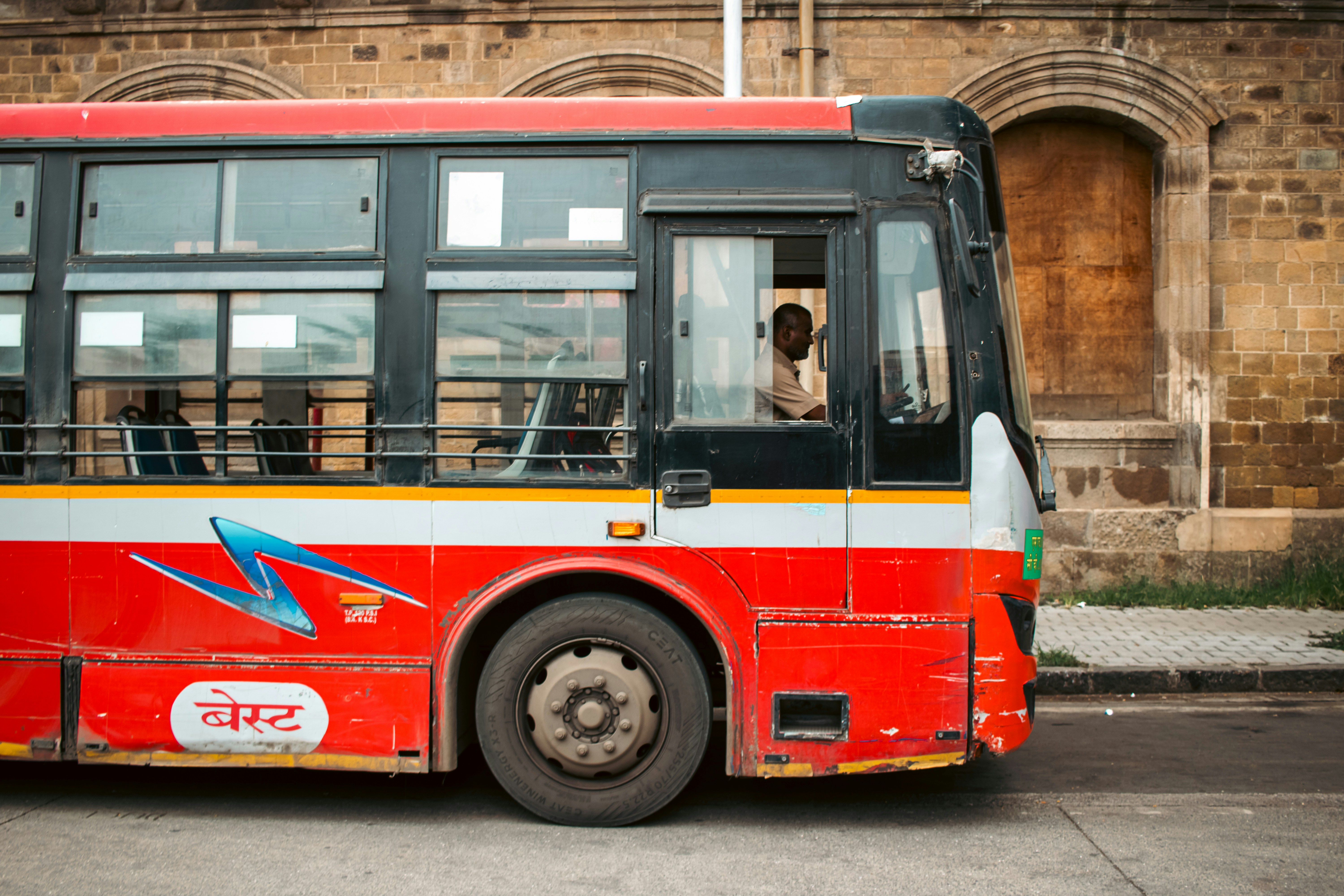 A red bus drives on the road with its driver.