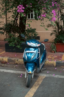 A blue scooter parks under flowers.
