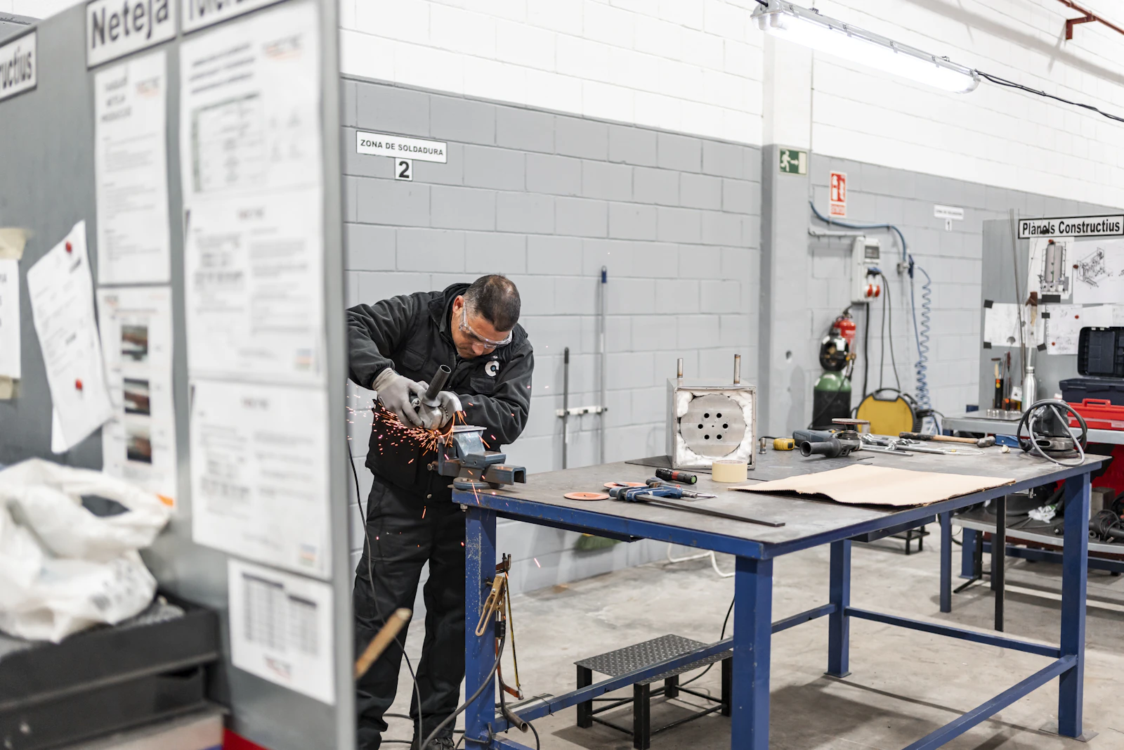 A trainee grinding metal in a workshop, sparks flying from the wheel