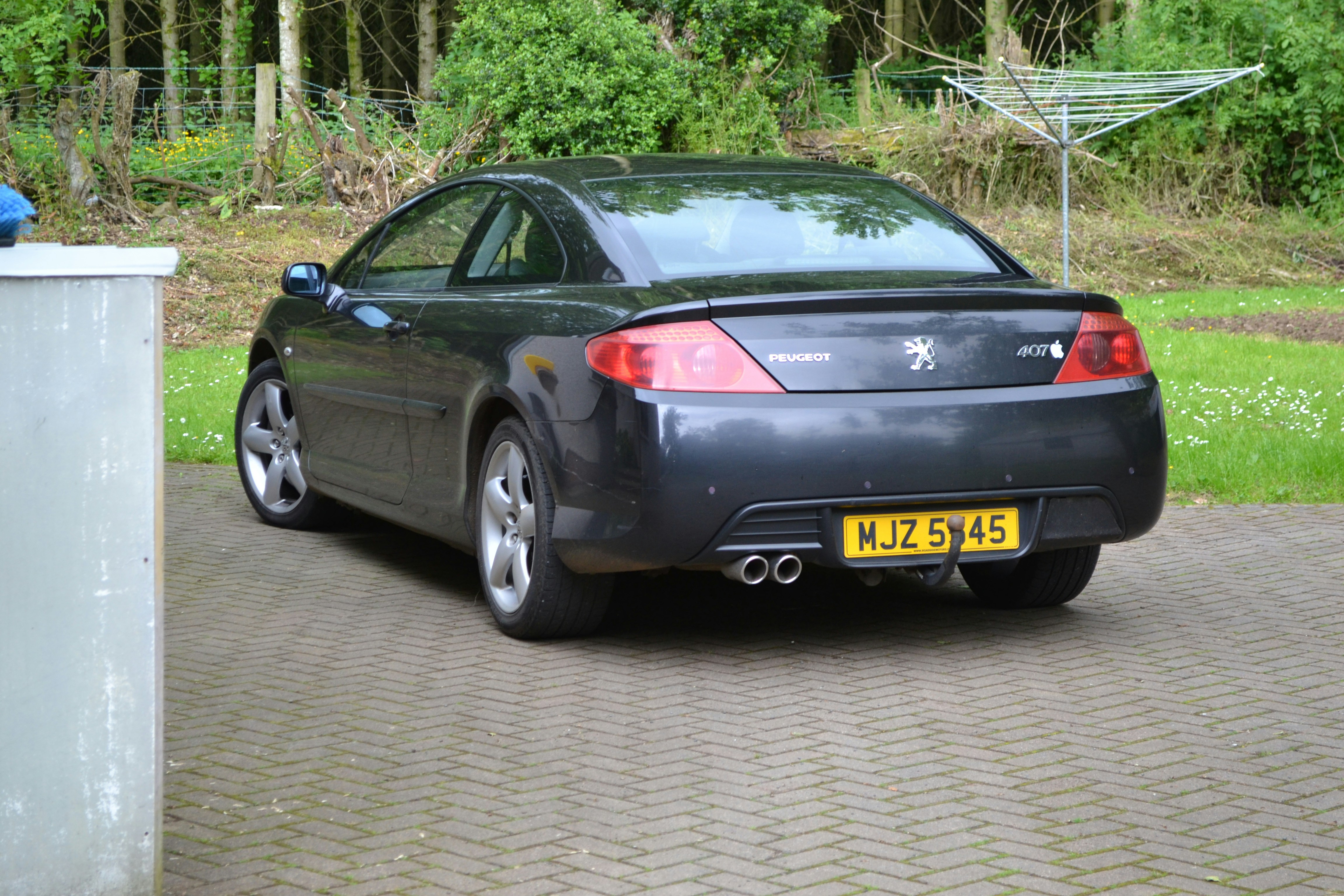 A dark peugeot car is parked outdoors.