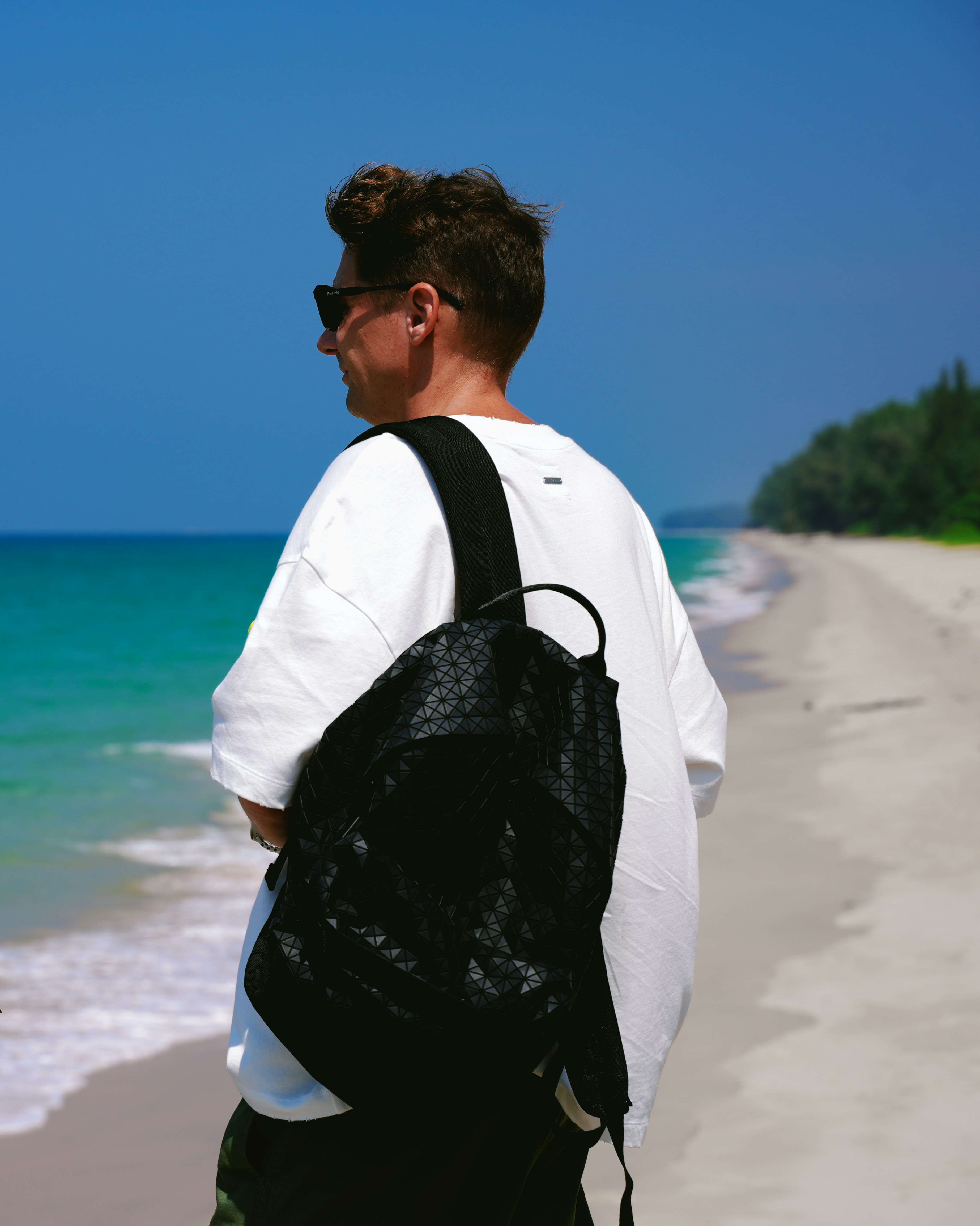 Man with backpack on a beach enjoys the view.