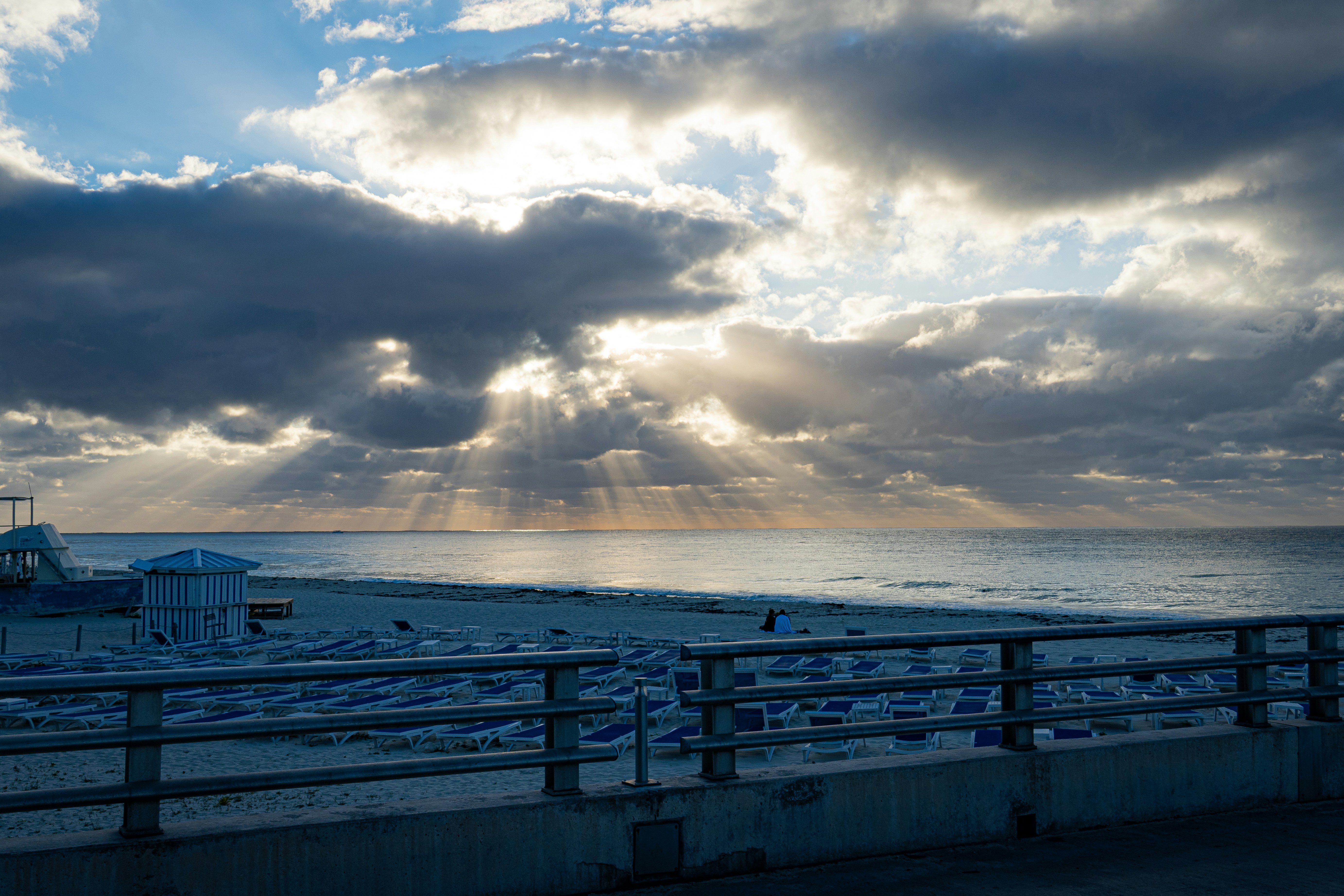 Sunlight pierces through stormy clouds over the beach.