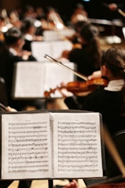 An orchestra performs, focusing on the sheet music.