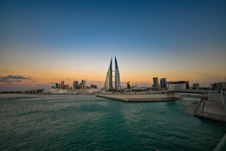 Modern buildings silhouetted at sunset over water.