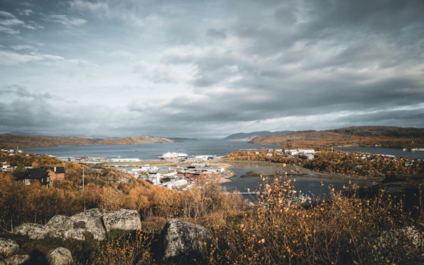 The town of Kirkenes and its fjord seen from a hillside in autumn, with a ship at the quay