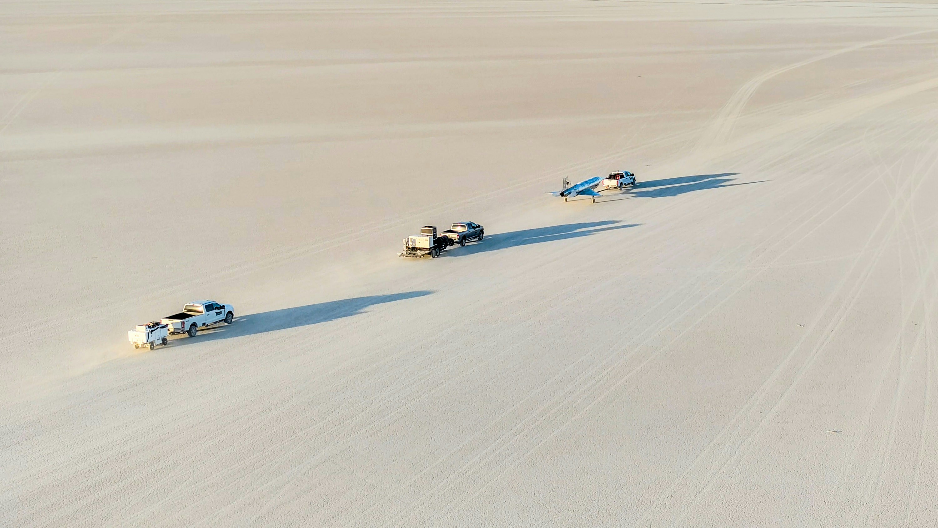 Four vehicles driving across a vast desert landscape.