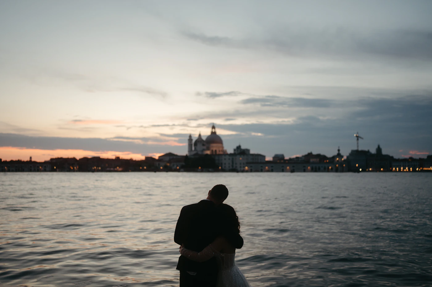 Couple sharing romantic elopement moment in silhouette against brilliant golden sunset reflected over calm water