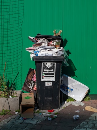 A black trash bin is overflowing with garbage.