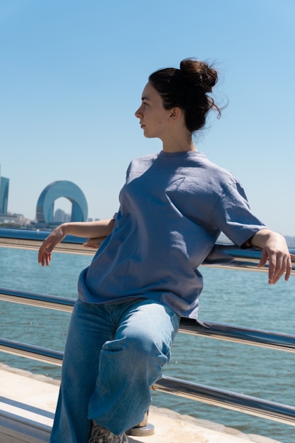Woman leans against a railing, gazing at the sea.