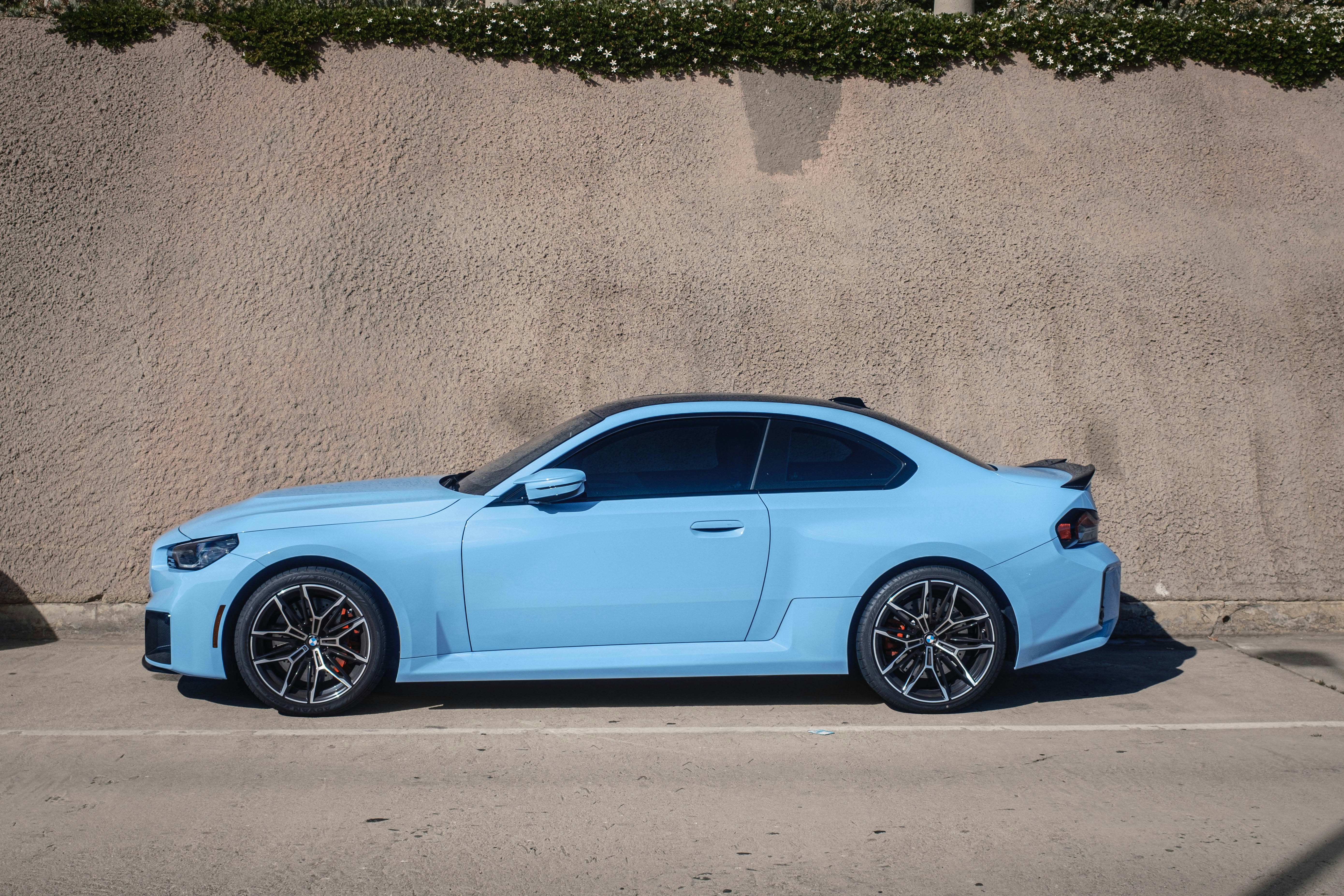 A blue sports car is parked beside a wall.