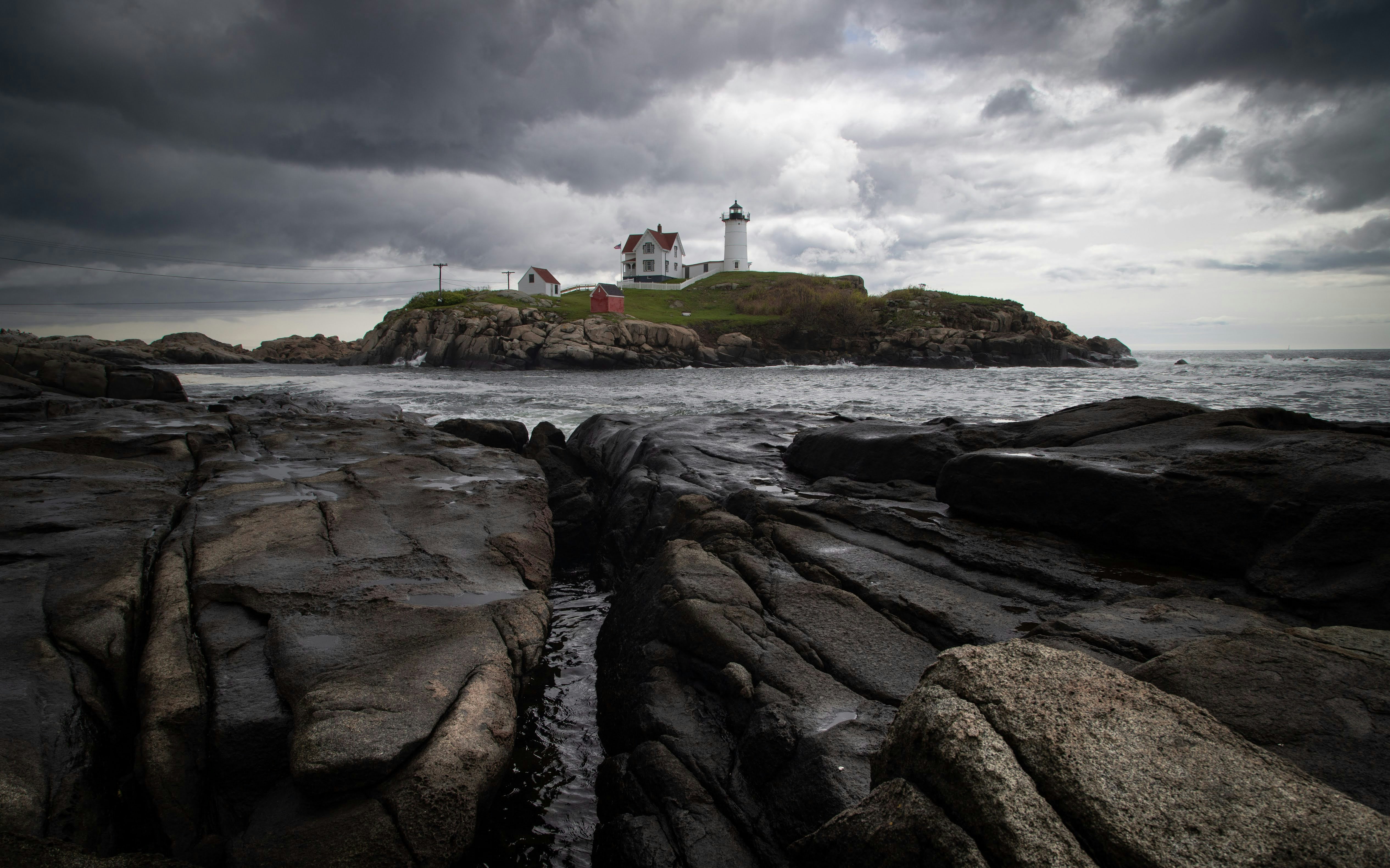 Lighthouse stands on a rocky island under stormy skies.