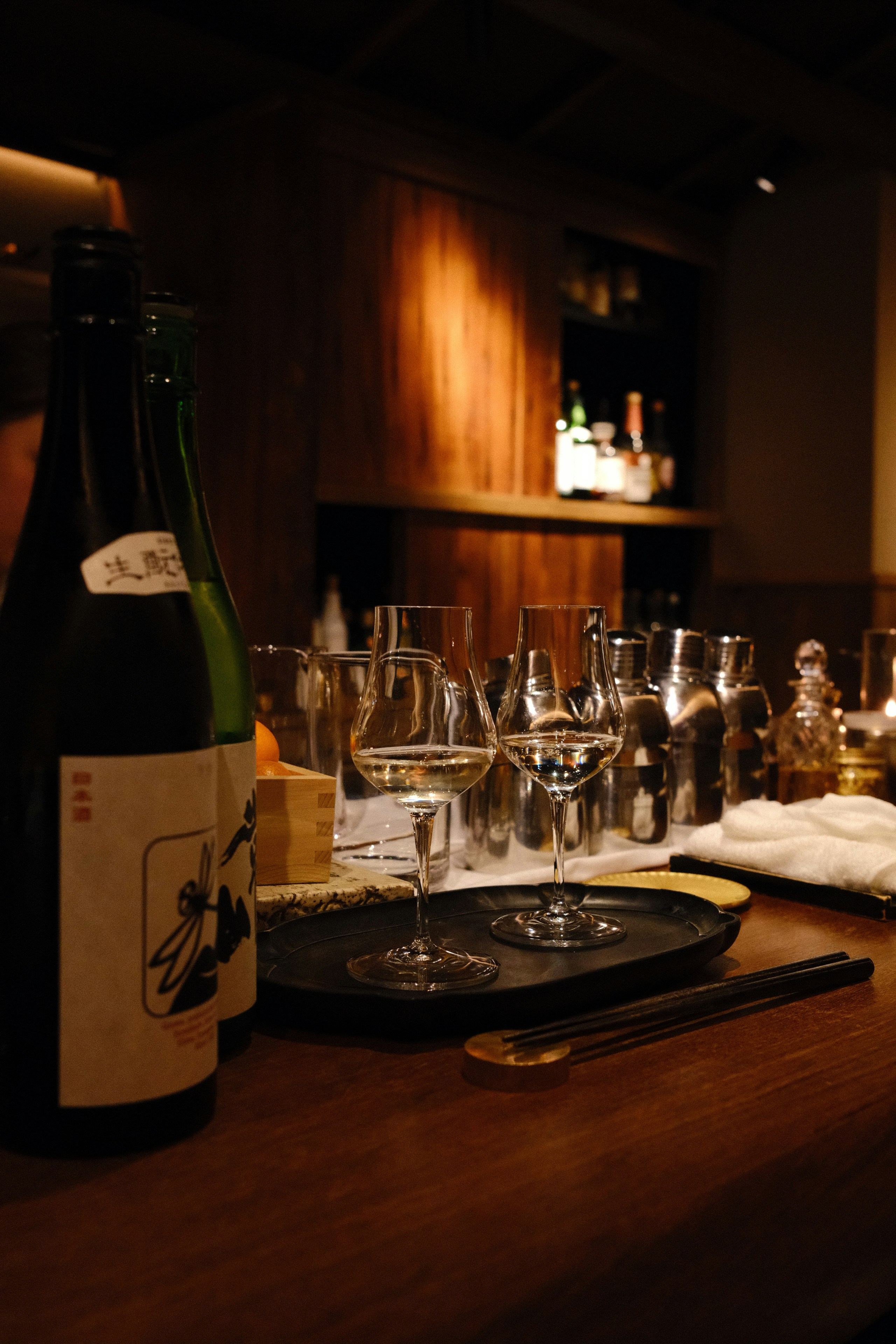 Sake bottles and glasses on a dimly lit bar.